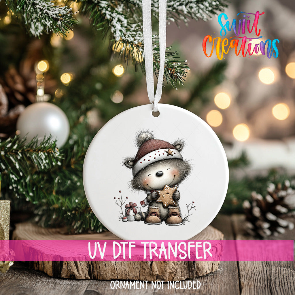 A white ornament with a cute cartoon bear wearing a hat and holding a star, hanging on a Christmas tree.