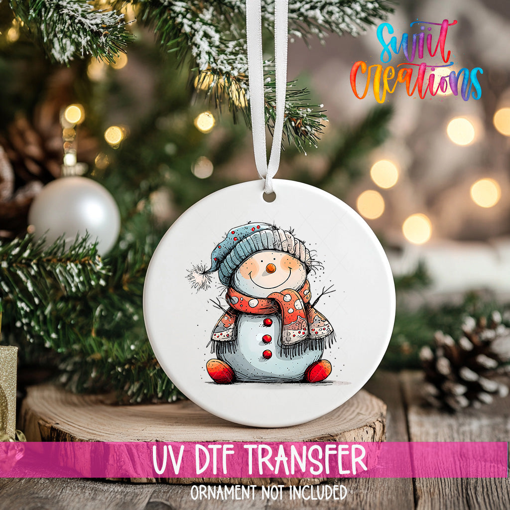 A white ceramic ornament featuring a smiling snowman is hanging on a Christmas tree.