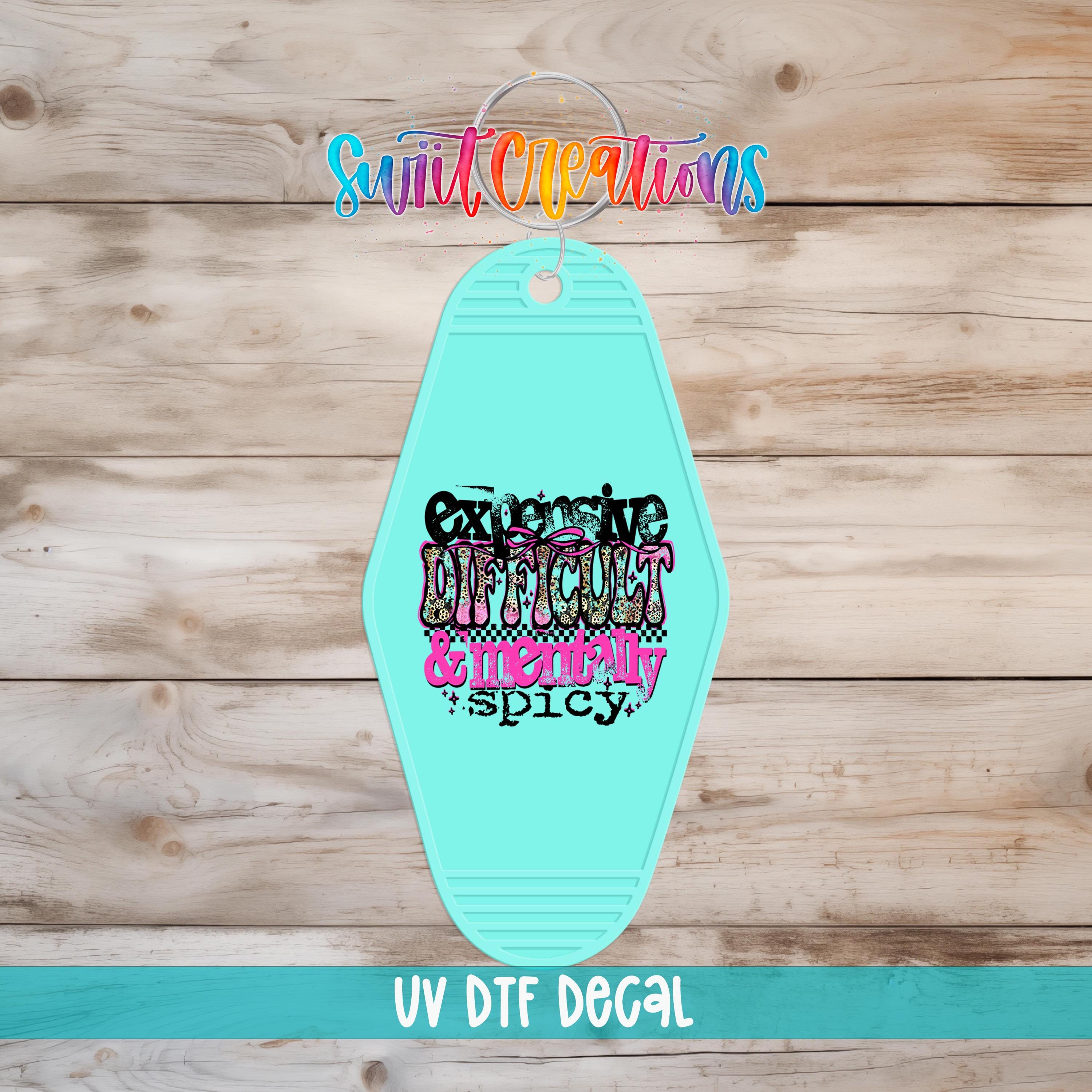A turquoise keychain with a colorful, stylized text design on it, placed on a wooden surface.
