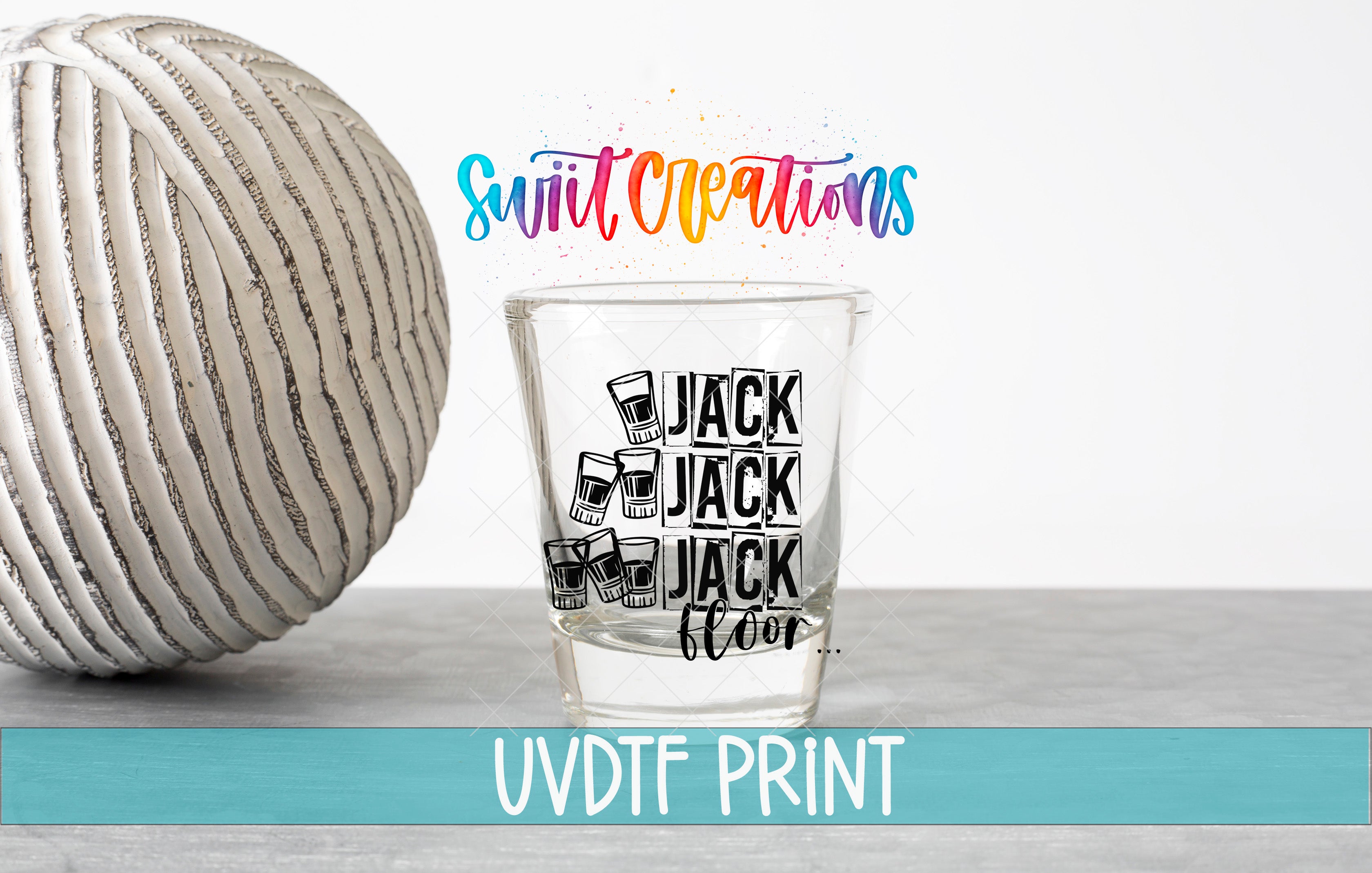 a shot glass with a design and text, placed next to a white ball on a gray surface.