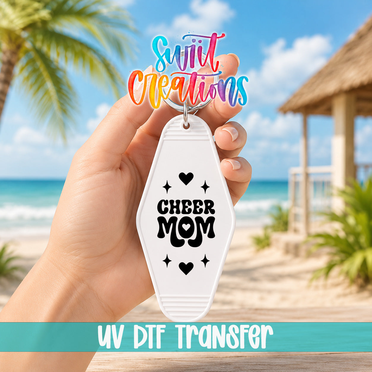 A hand holding a keychain with the text "Cheer Mom" printed on it, with a beach and palm trees in the background.