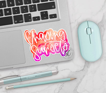 Chasing Sunsets vinyl sticker on a silver laptop next to a mint mouse and pens