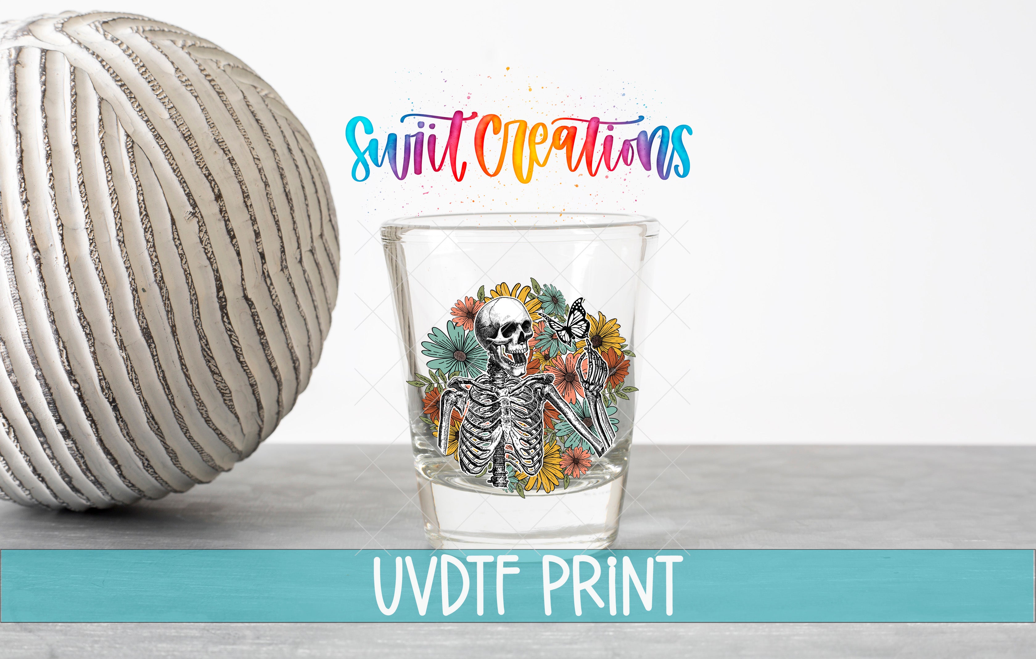 a glass with a skeleton design and flowers, placed next to a white ball with a striped pattern. The text above the glass reads "Swift Creations" and "UVDF PRINT".