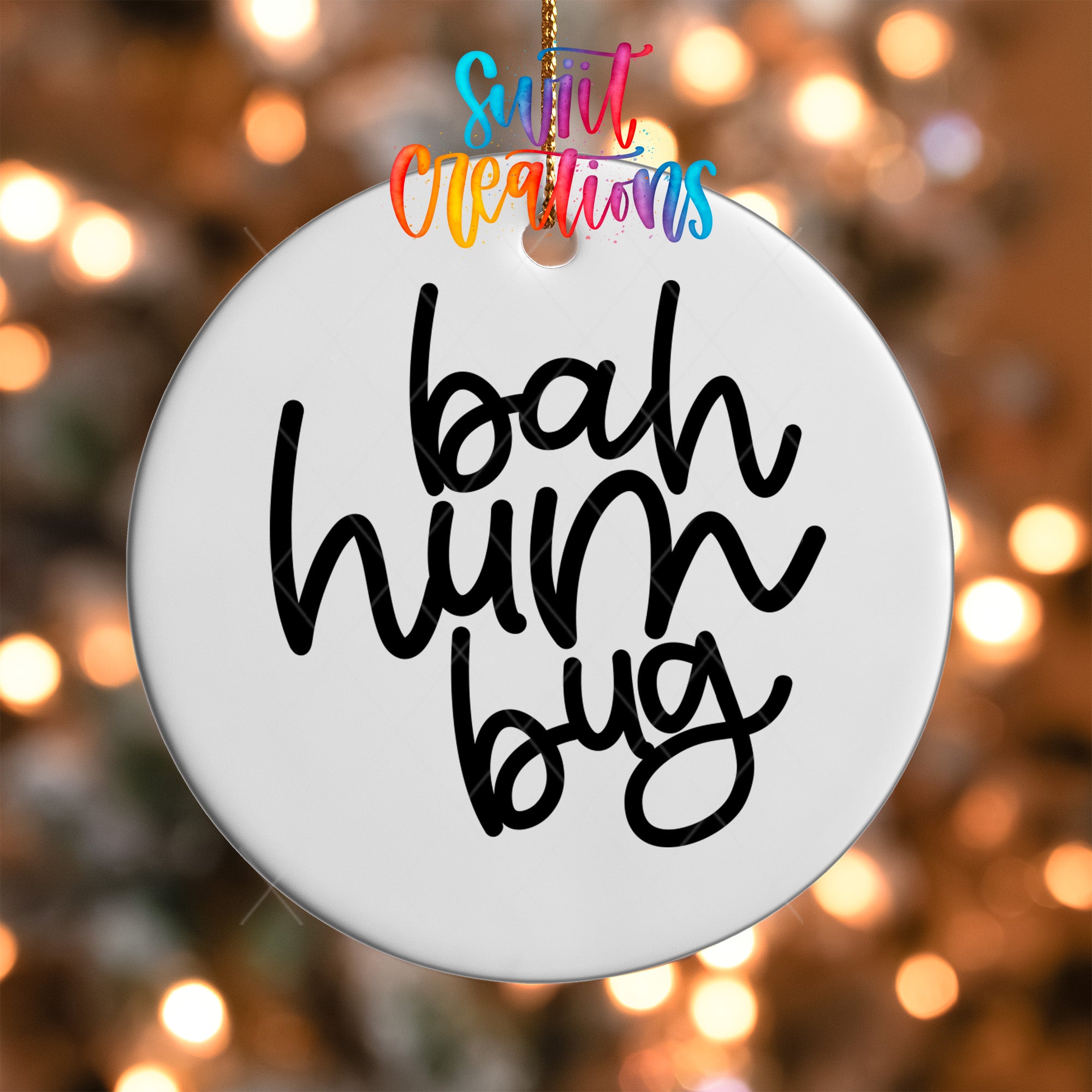 A white ornament with the text "bah hum bug" written on it, hanging against a background of colorful lights.