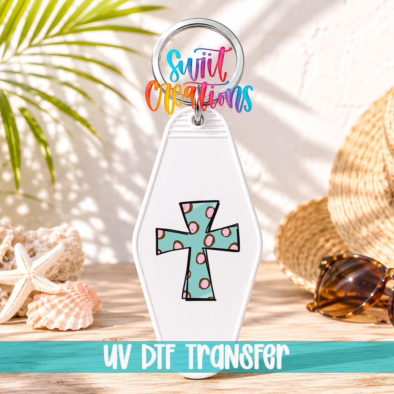 A keychain with a colorful cross design and the text "UV DDF Transfer" is displayed on a wooden surface, surrounded by sunglasses and a straw hat.