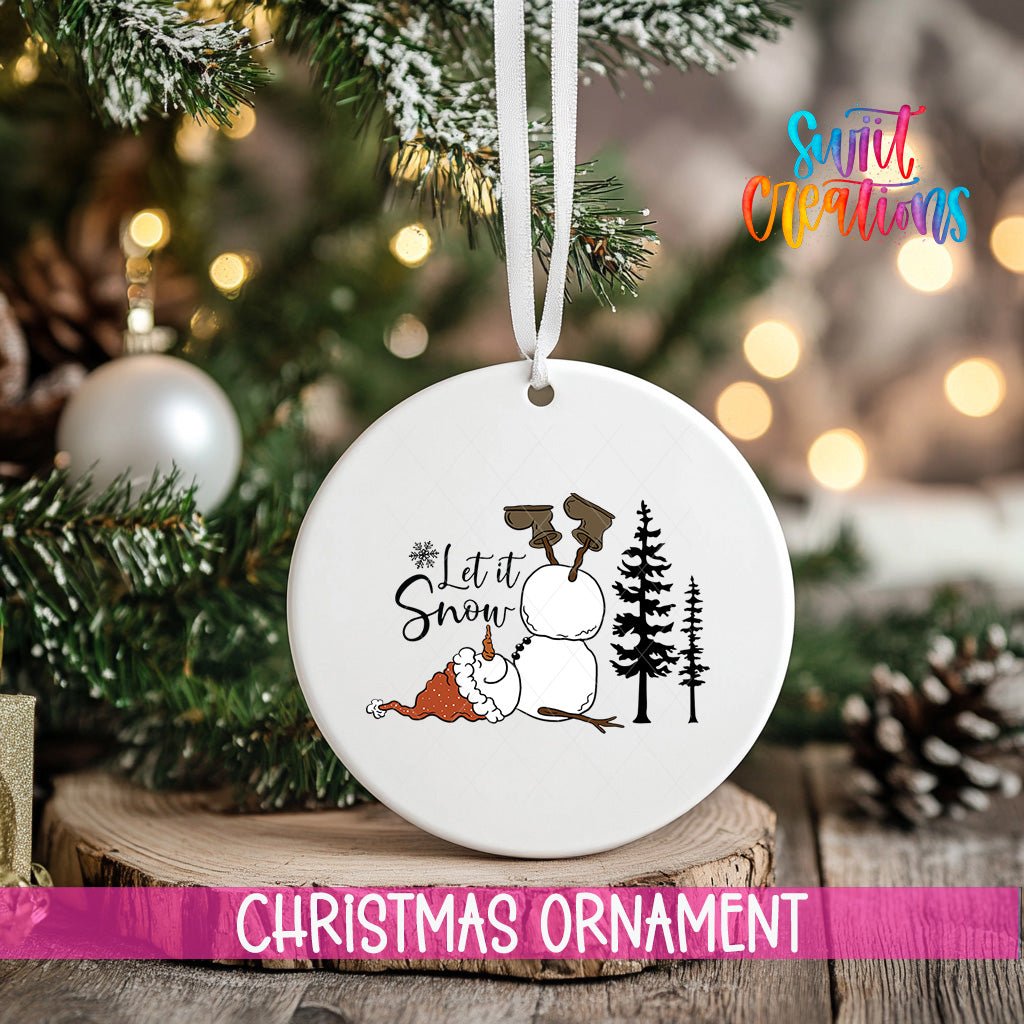 A white Christmas ornament with a snowman and the text "Let it Snow" is hanging on a tree, surrounded by pine branches and other holiday decorations.