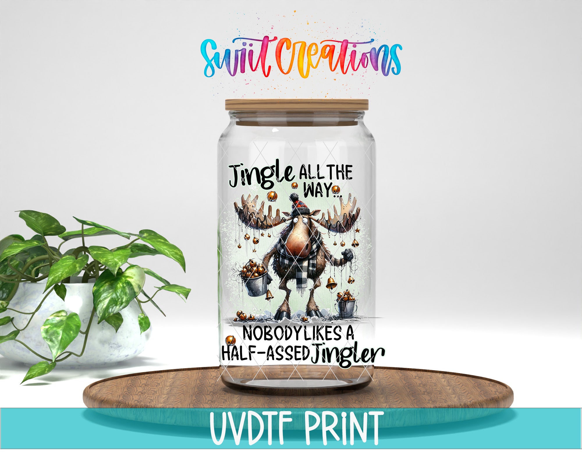 A glass jar with a moose illustration and text, placed on a wooden surface next to a potted plant.