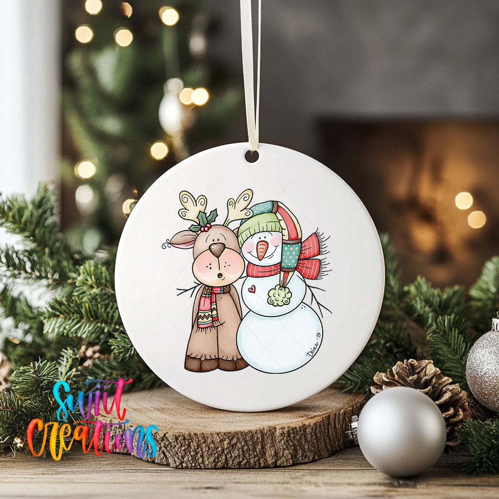 A white ceramic ornament featuring a reindeer and a snowman, with a Christmas tree in the background.