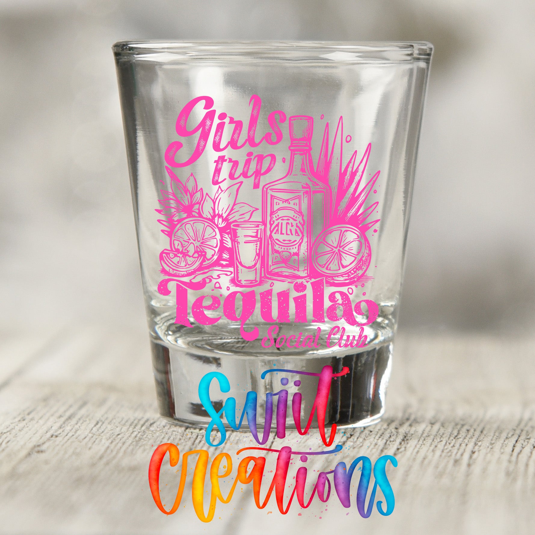 A shot glass with a pink and purple design featuring text and illustrations related to tequila, such as a tequila bottle, lime, and orange slices.