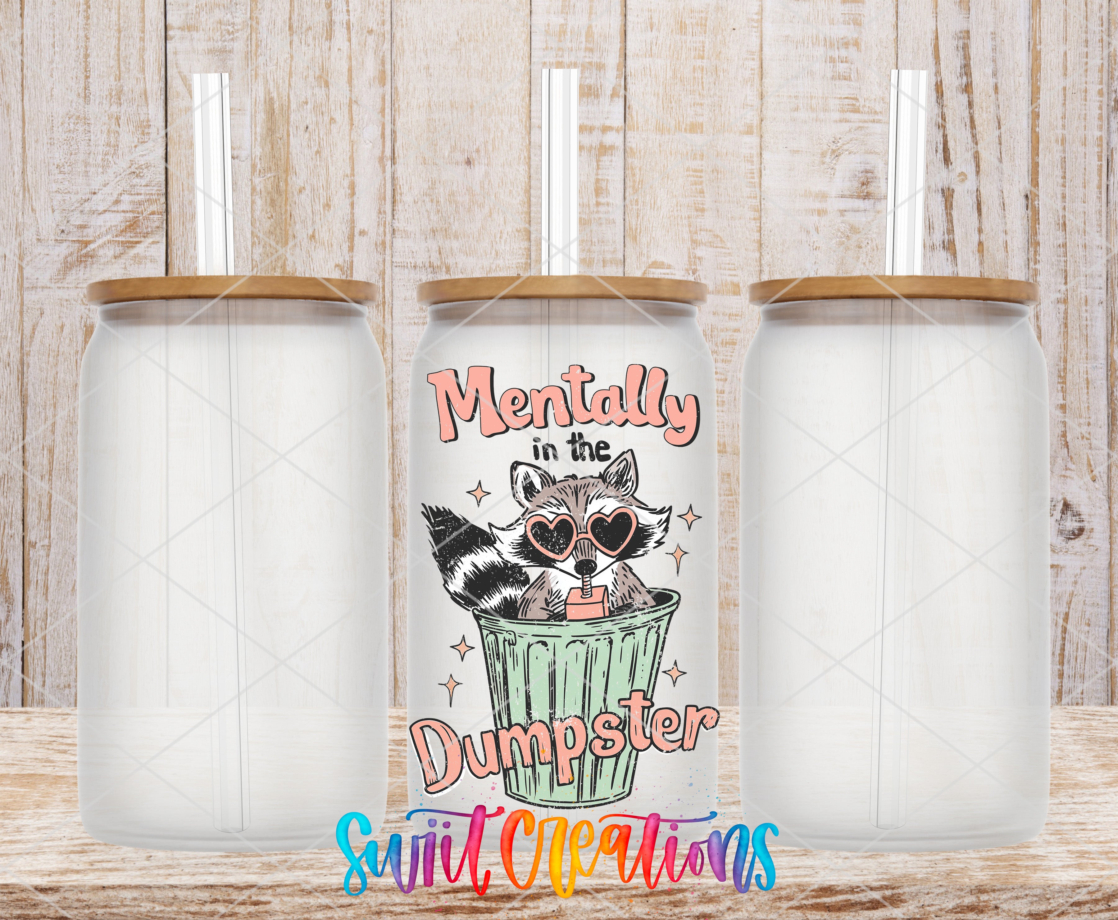 three clear glass tumblers with straws, each with a lid and a printed design on the front. The design includes a raccoon wearing sunglasses and the text "Mentally in the Dumpster" in a playful, colorful style.