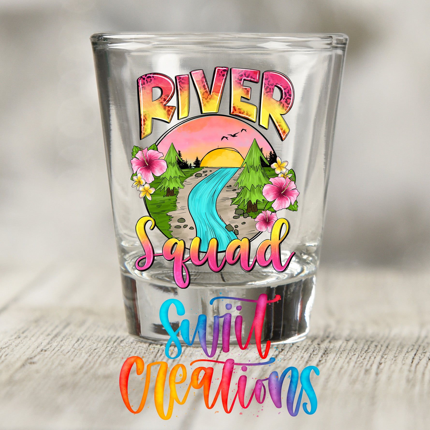 A shot glass with a colorful design featuring a river, flowers, and a sunset.