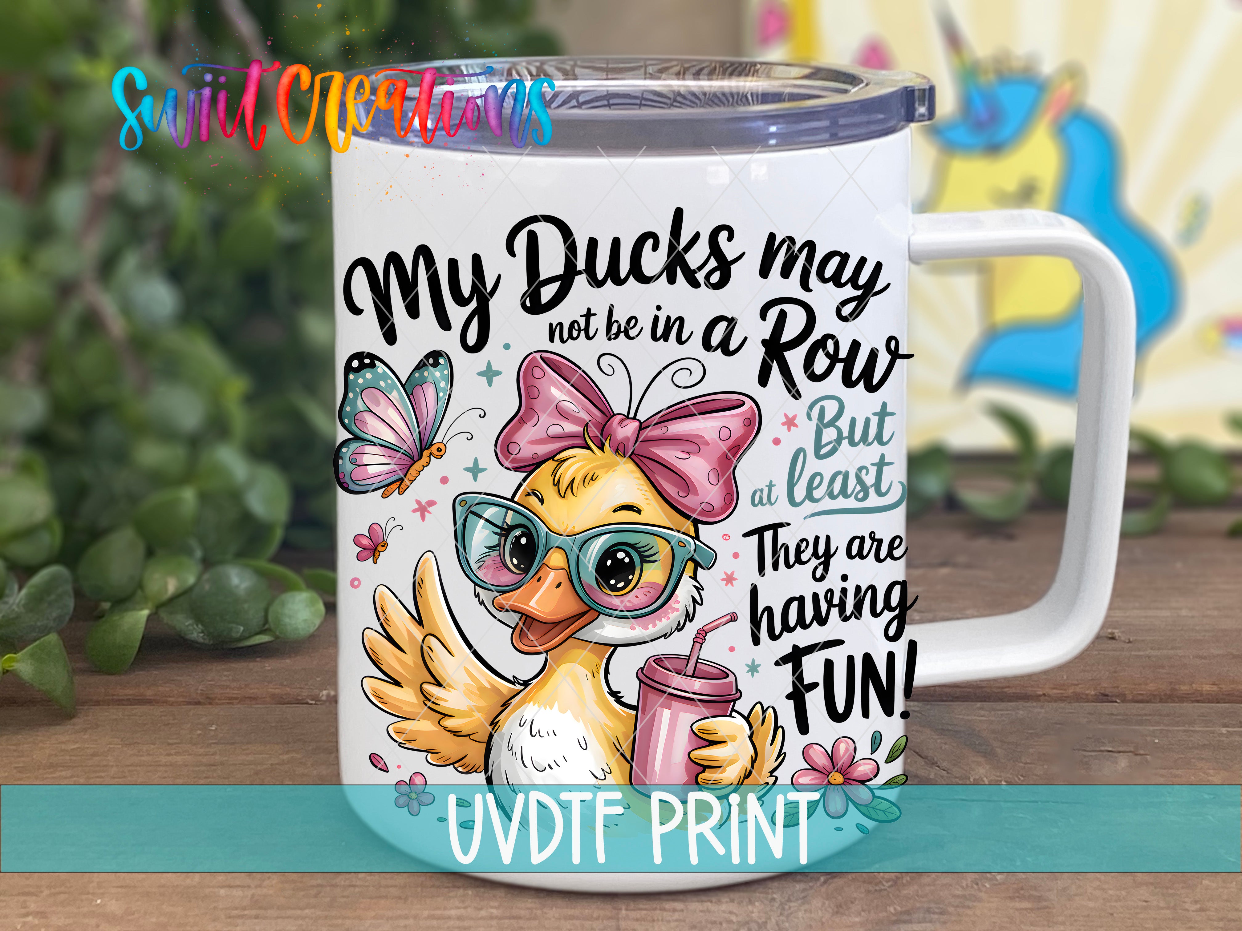 A white mug with a cartoon duck wearing glasses and a pink bow, along with text and illustrations, placed on a wooden surface.