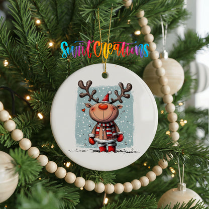 A white ceramic ornament featuring a cartoon reindeer is hanging on a Christmas tree, surrounded by ornaments and lights.