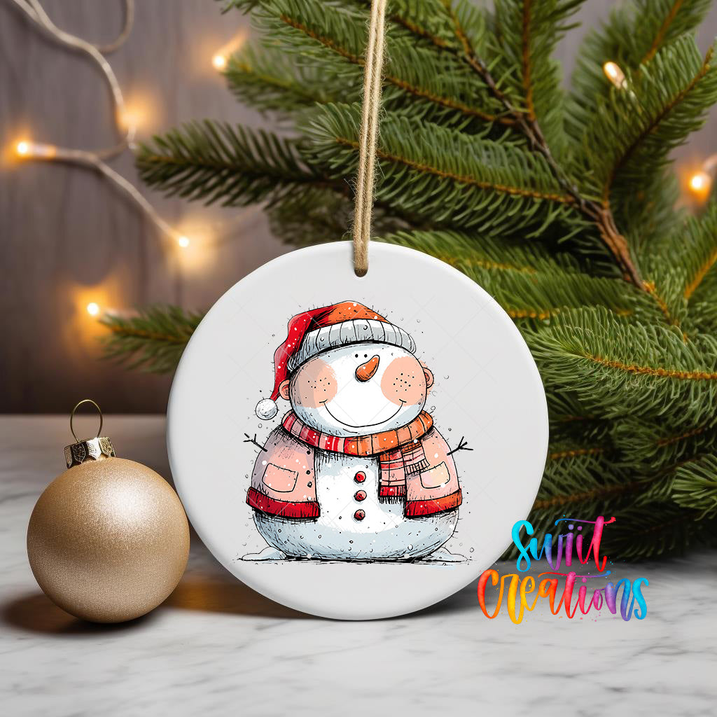 A white ceramic ornament featuring a snowman is displayed on a table, with a gold ornament and a Christmas tree in the background.