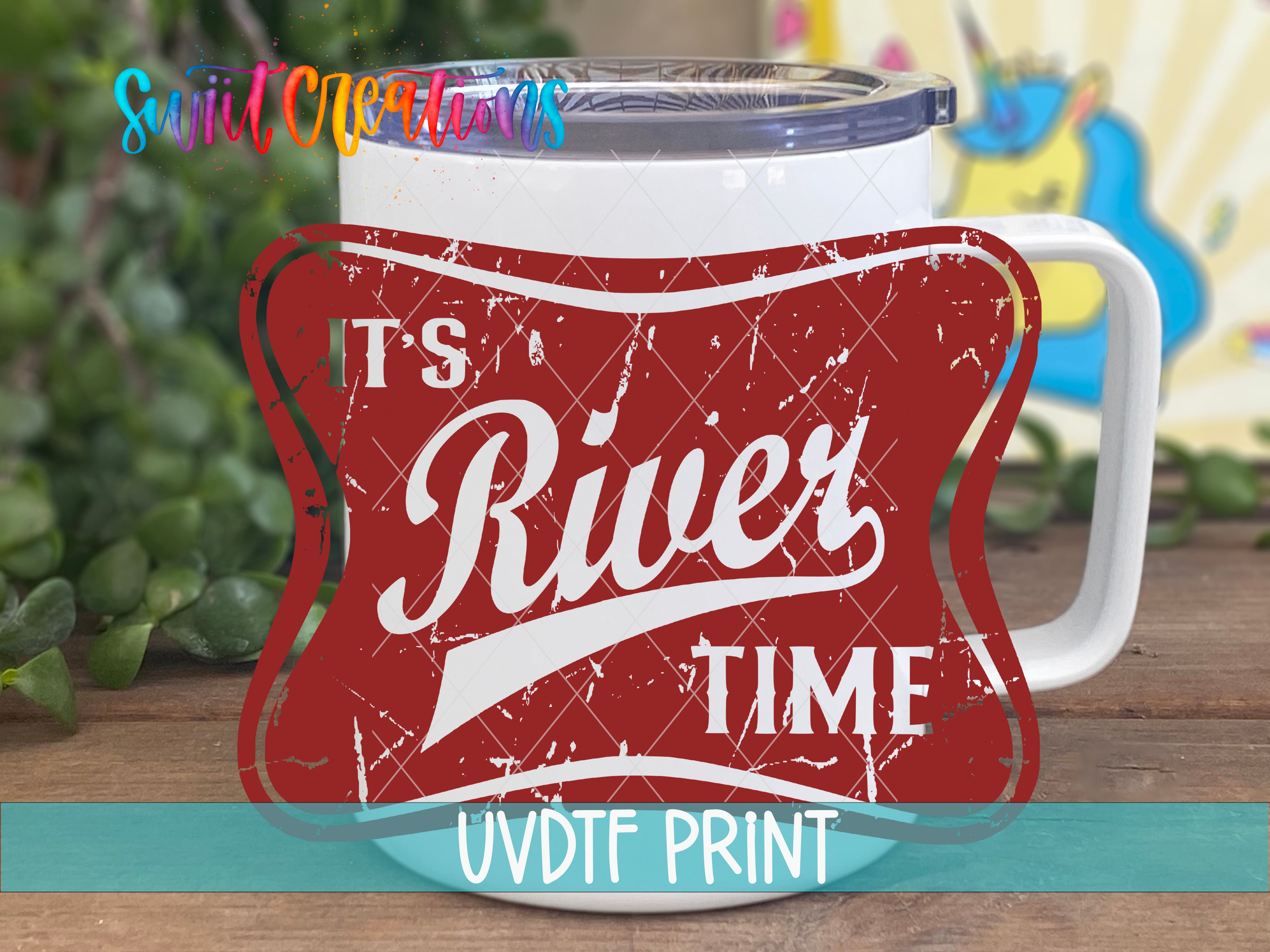 A white mug with a red and white label that says "River Time" and "UVDF PRINT" printed on it, placed on a wooden surface with green leaves in the background.