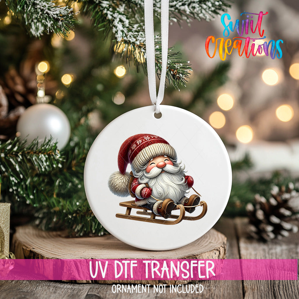 A white ornament with a Santa Claus image is hanging on a Christmas tree, with a blurred background of pine branches and twinkling lights.