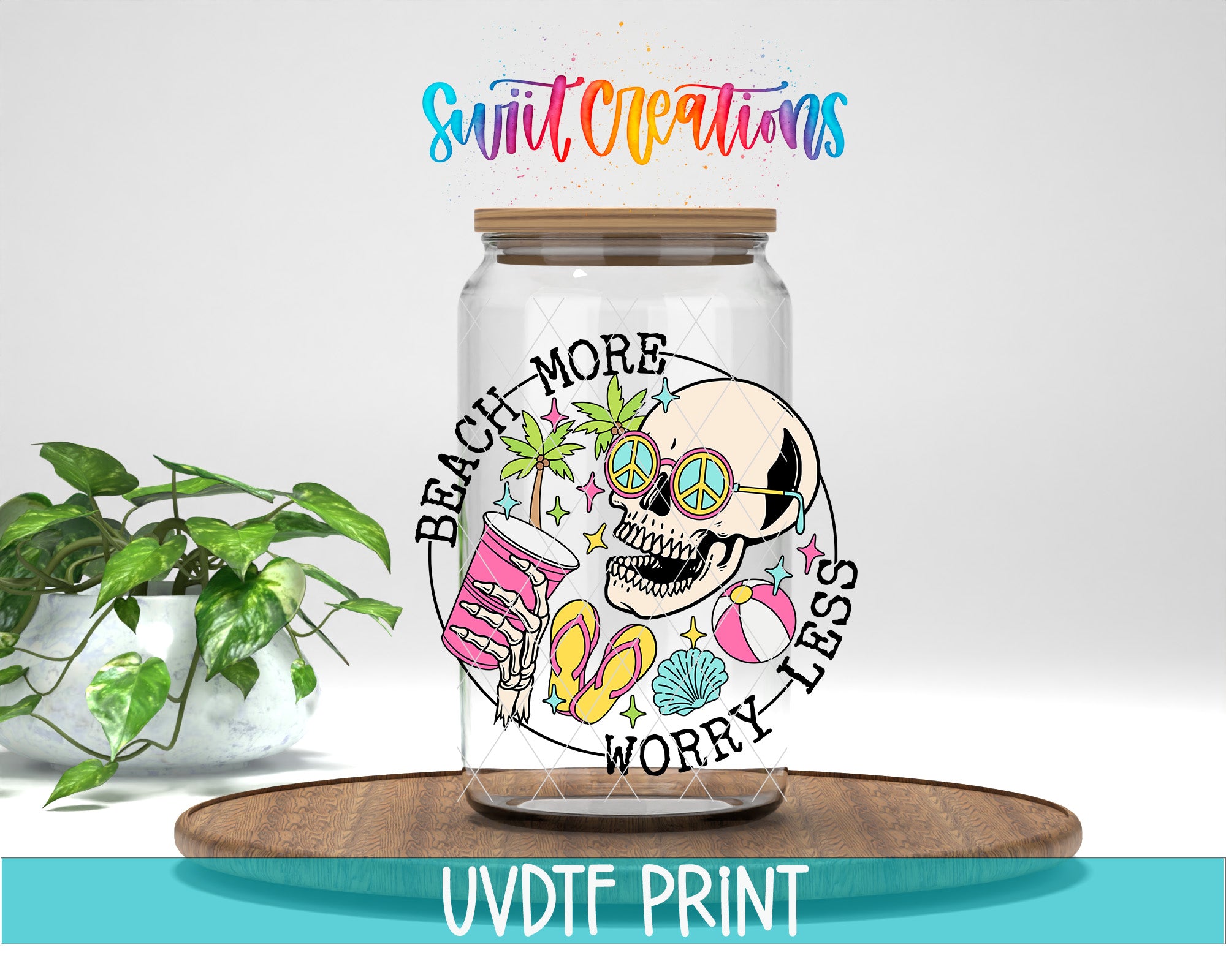 A glass jar with a colorful design featuring a skull, sunglasses, beach-themed items, and the text "Beach More Worry Less" printed on it. The jar is placed on a wooden surface, and there is a potted plant in the background.