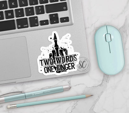 Two Words One Finger vinyl sticker on a silver laptop next to a mint mouse and pens