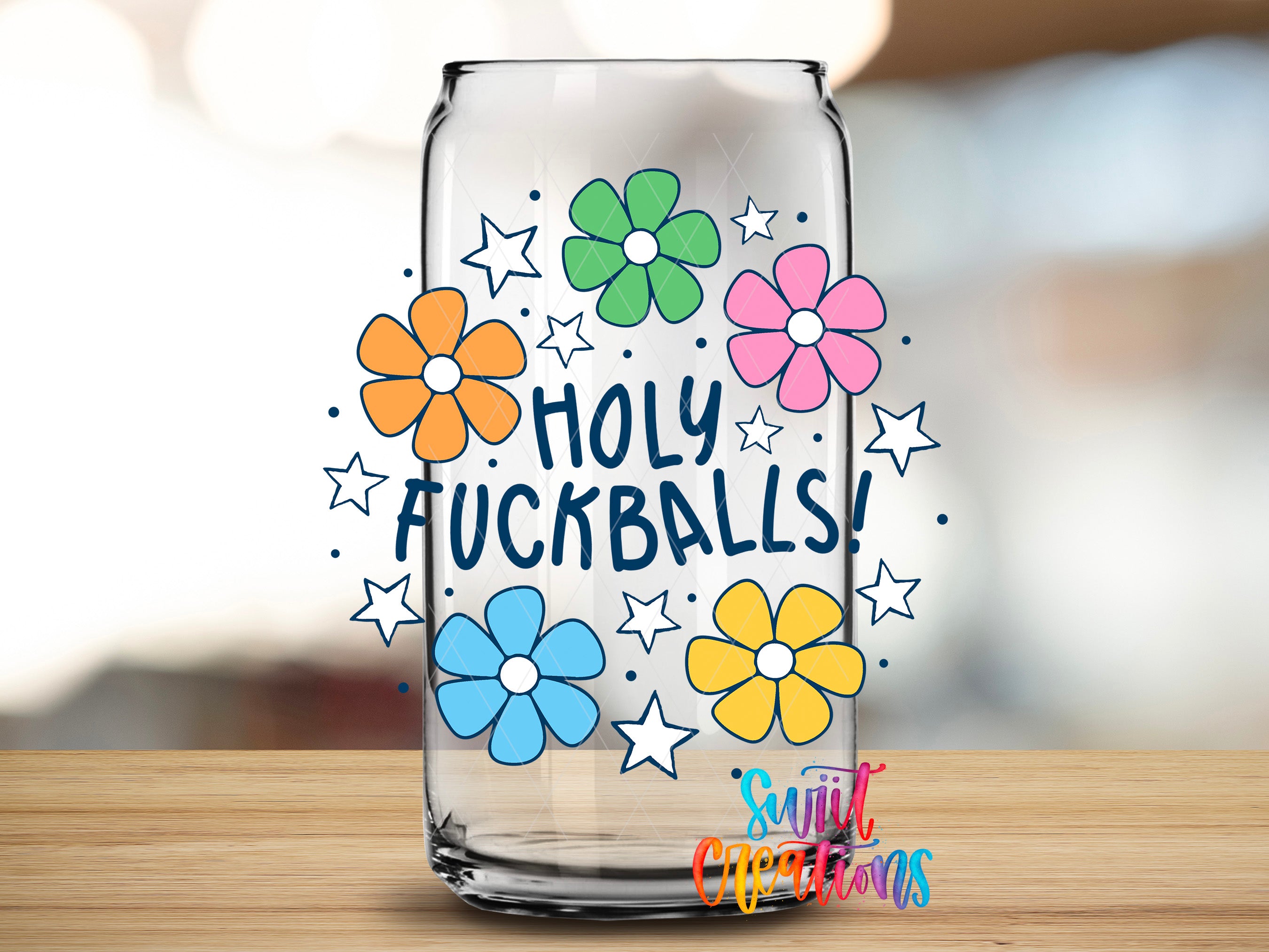 A clear glass can with a colorful design featuring flowers and stars, along with the text "HOLY FUCKBALLS!" written in a playful font.