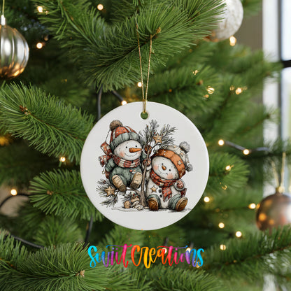 A white ceramic ornament featuring two snowmen is hanging on a Christmas tree, surrounded by other ornaments and lights.