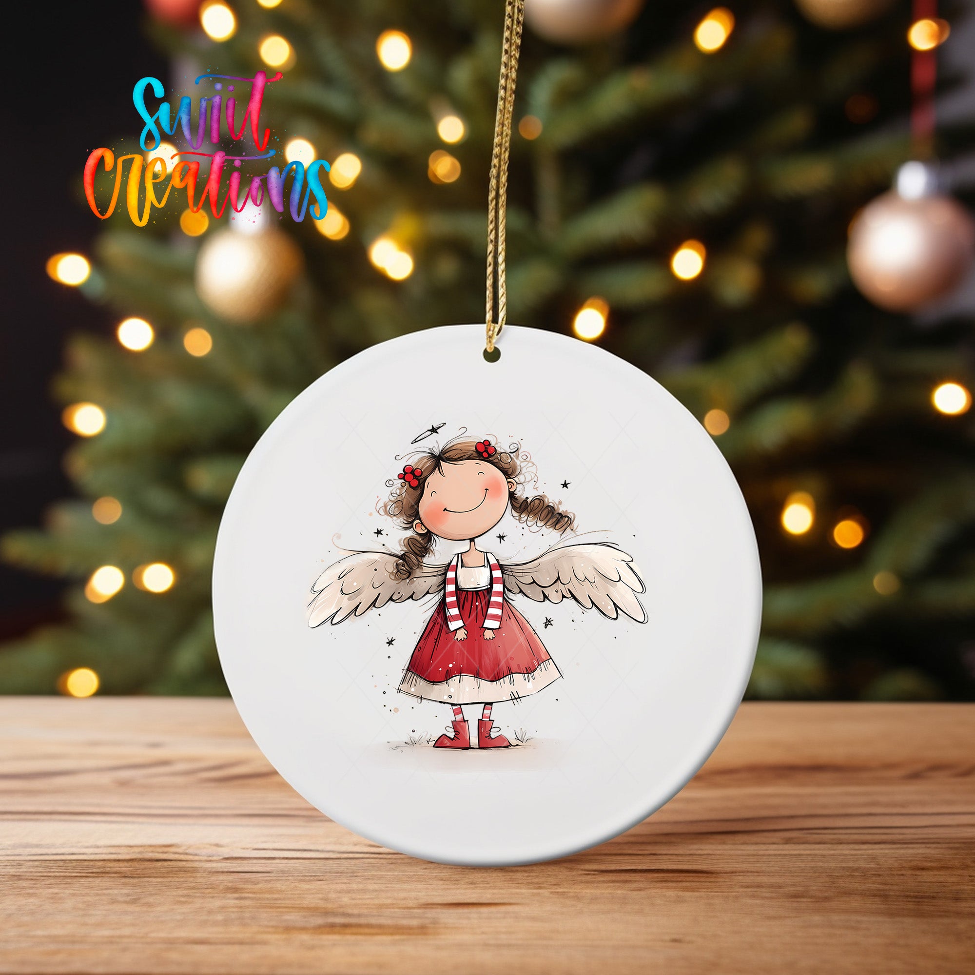 A white ceramic ornament featuring a smiling girl with wings, hanging on a string in front of a blurred Christmas tree with twinkling lights.