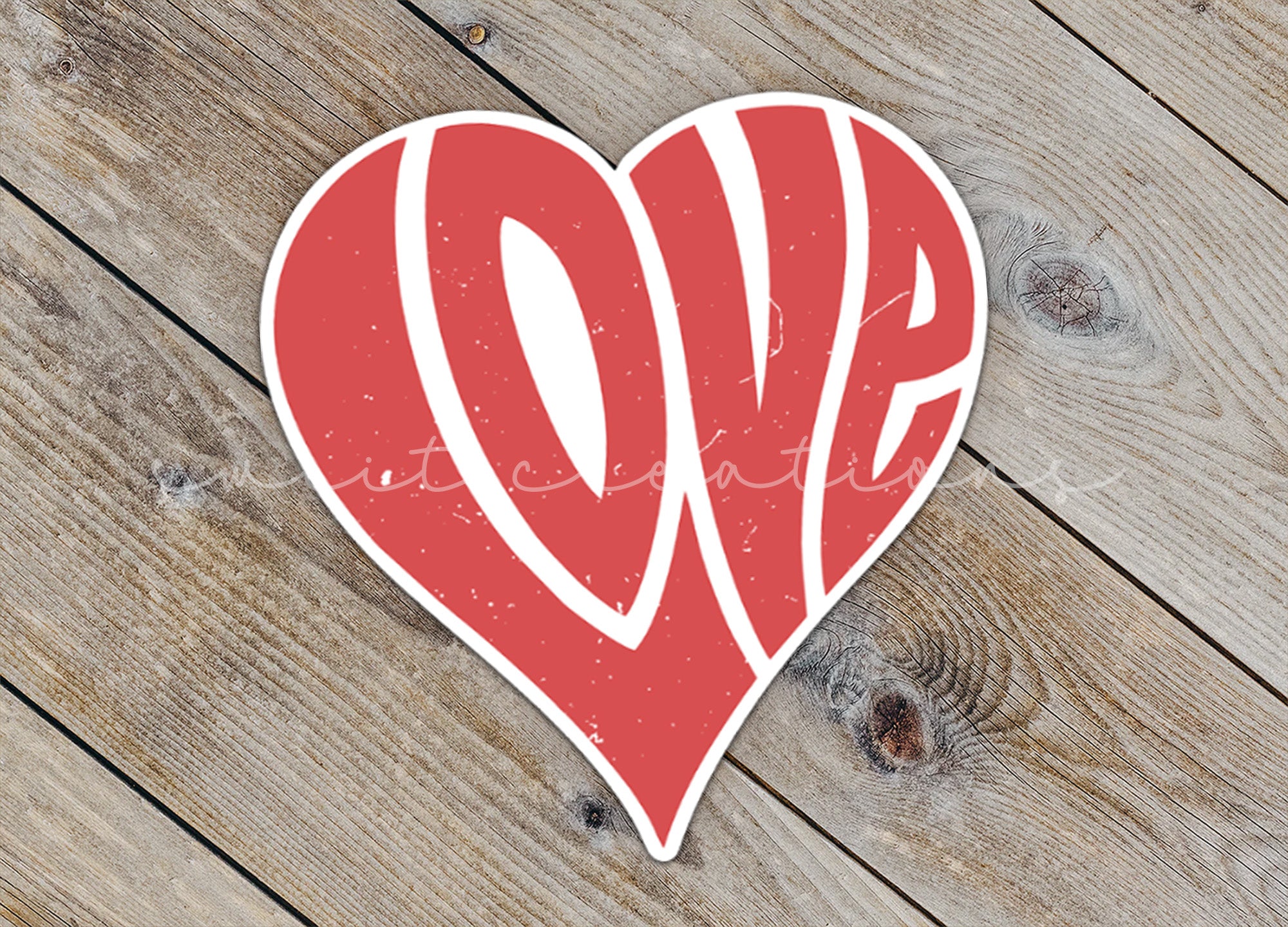 a red heart shaped sticker sitting on top of a wooden floor