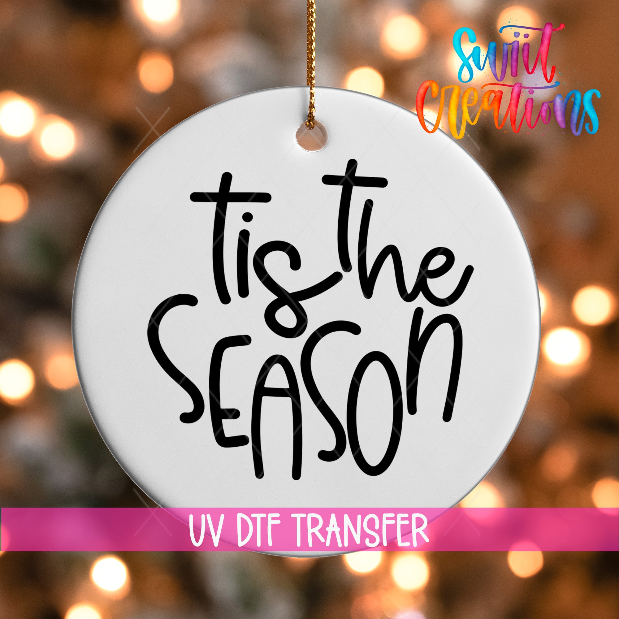 A white circular ornament with the text "Tis the SEASON" written on it, hanging against a background of colorful lights.