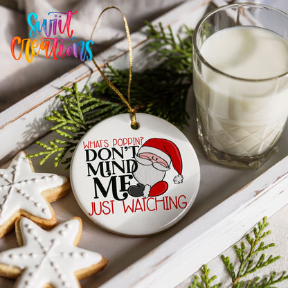 a Christmas ornament with a Santa Claus design, a glass of milk, and some cookies on a white tray.