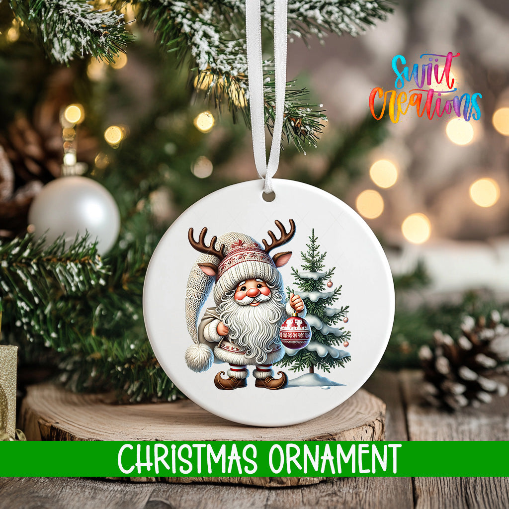 A white Christmas ornament featuring a Santa Claus figure holding a Christmas ornament and a pine tree, with a blurred background of a decorated Christmas tree and twinkling lights.