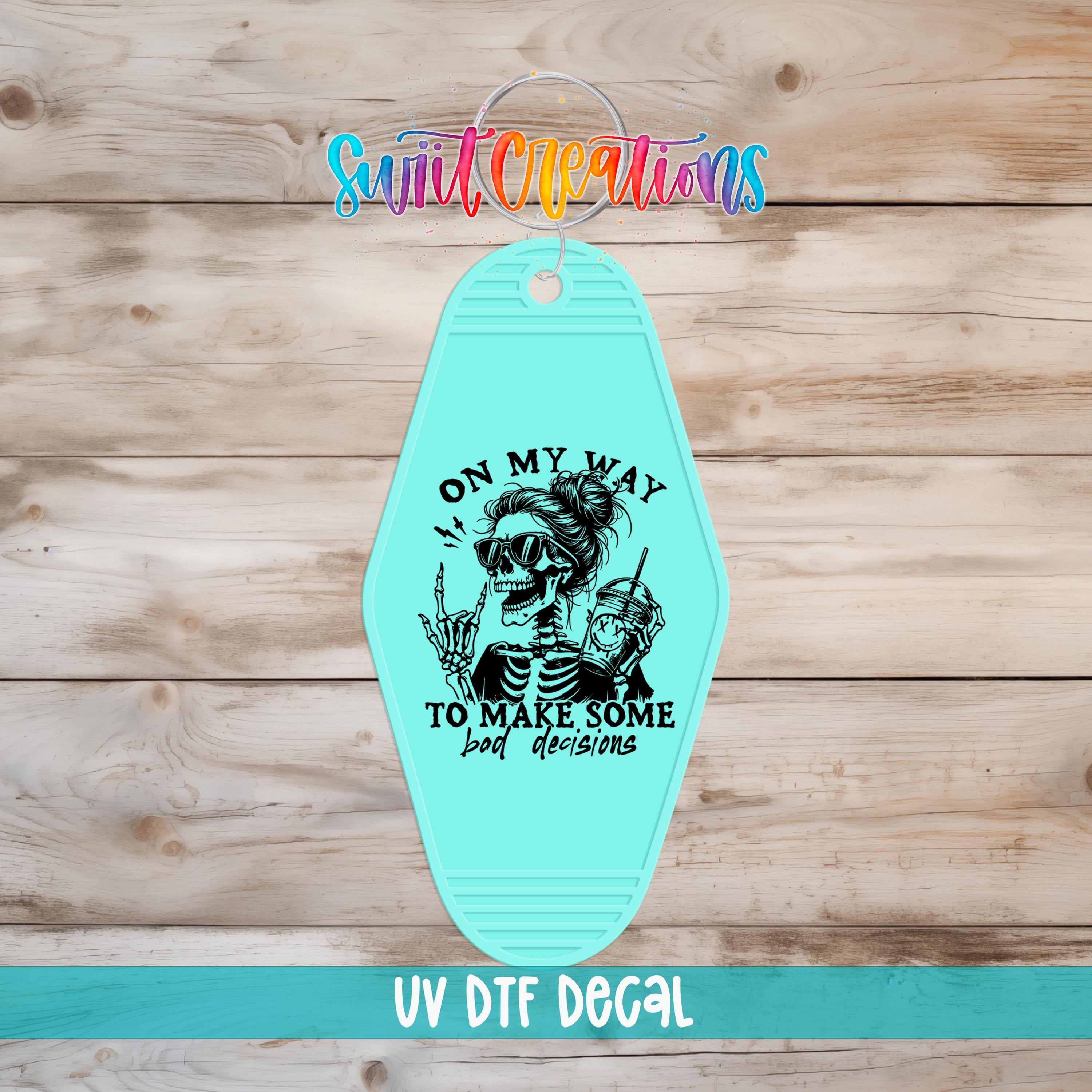 A turquoise keychain with a skeleton graphic and the text "I ON MY WAY TO MAKE SOME BAD DECISIONS" printed on it.