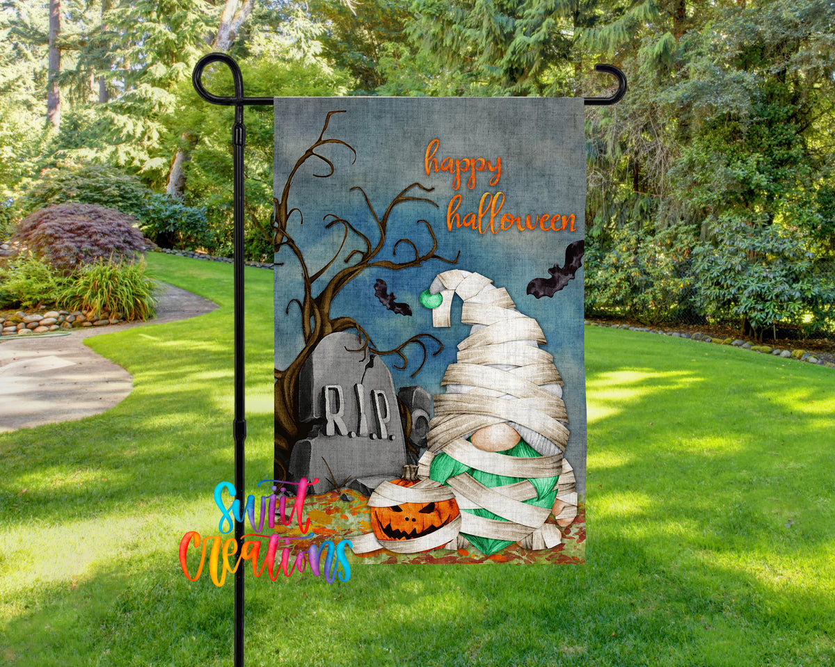 A Halloween-themed garden flag featuring a gnome wrapped in bandages, a carved pumpkin, and a gravestone with bats flying around it.