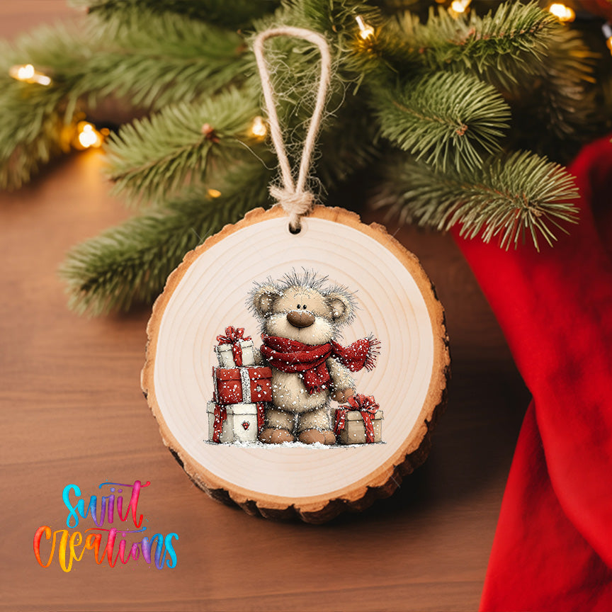 A wooden ornament with a teddy bear wearing a red scarf and holding presents, hanging on a Christmas tree.