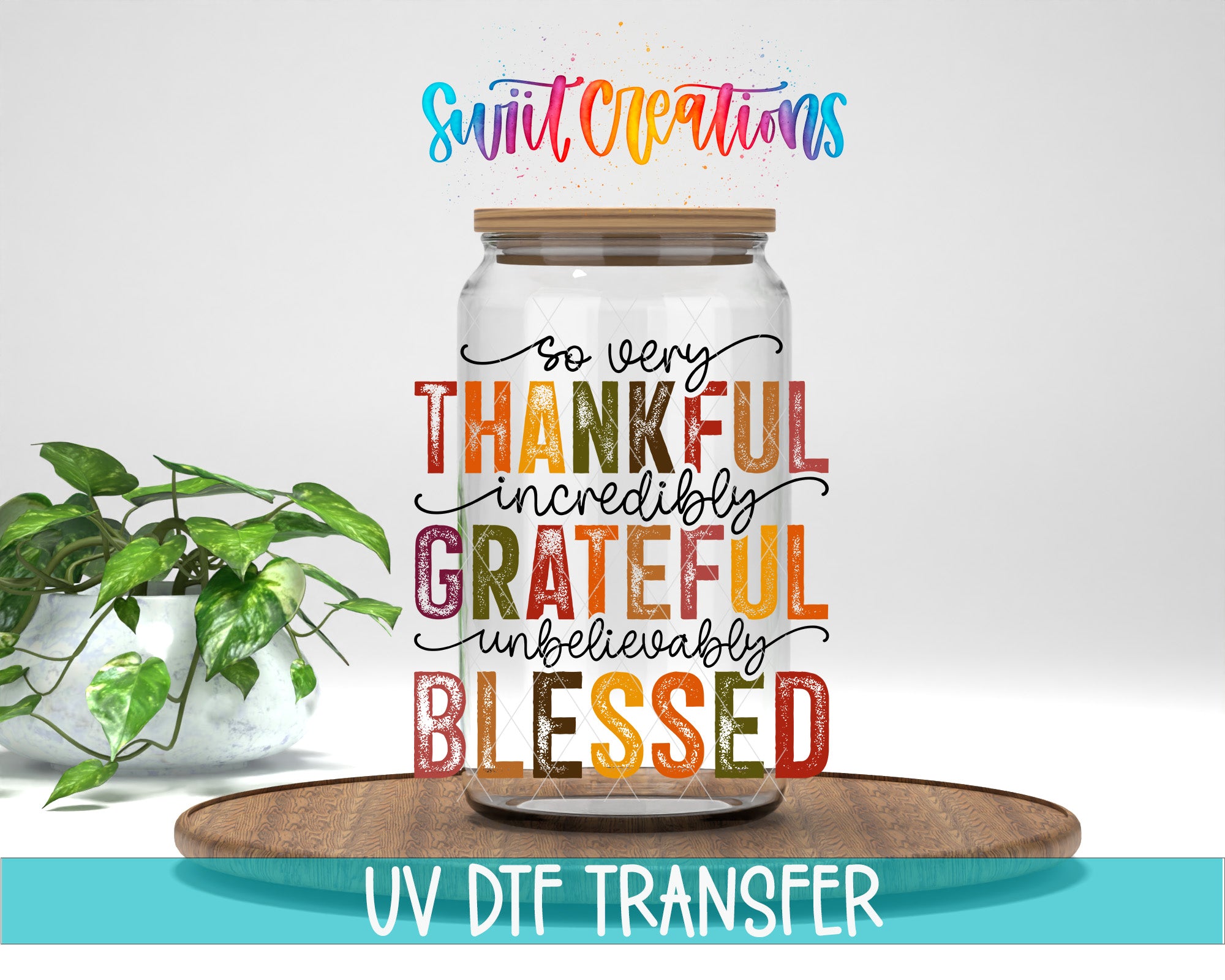 A glass jar with a wooden lid, filled with a colorful liquid, sits on a wooden surface. The jar has a message written on it that says "So very THANKFUL incredibly GRATEFUL incredibly BLESSED". The background is plain white, and there is a potted plant to the left of the jar.
