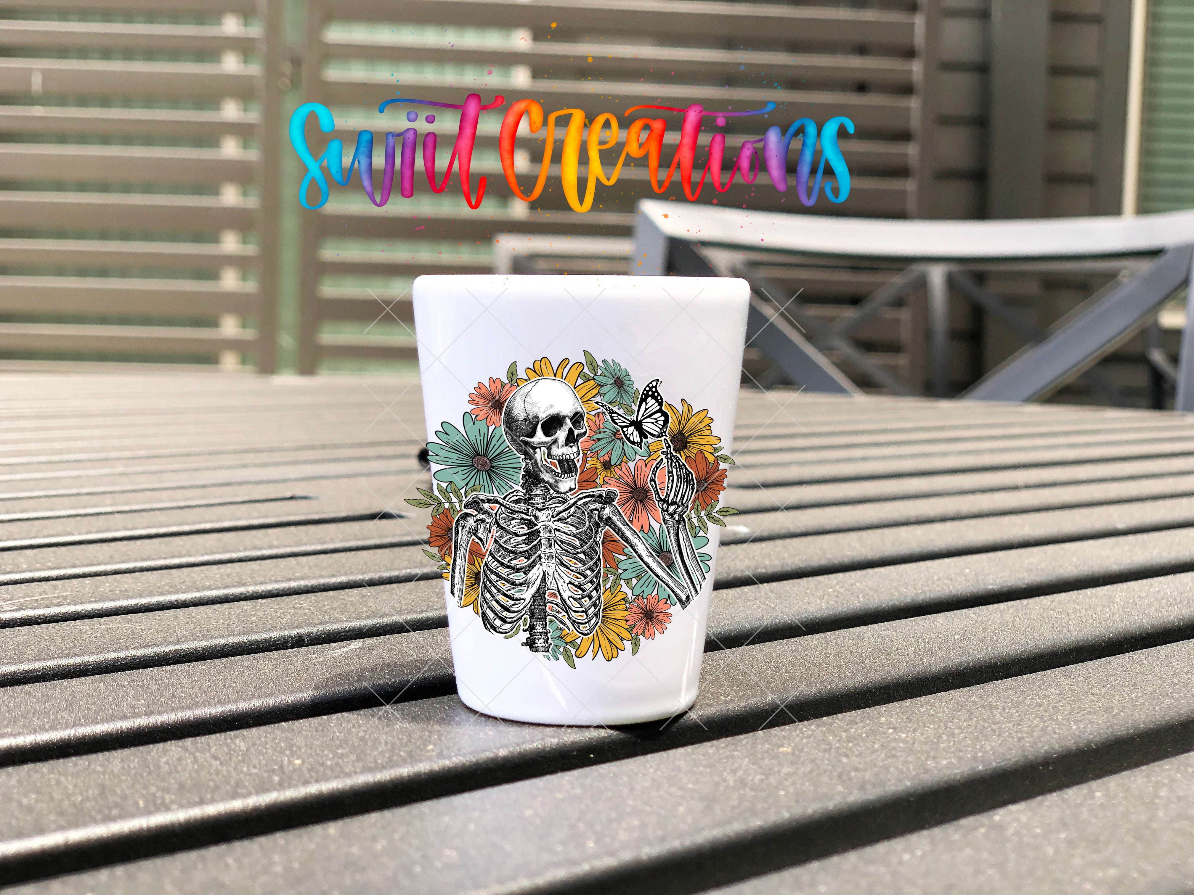 A white ceramic mug with a colorful floral design and a skeleton figure on it, placed on a wooden surface.
