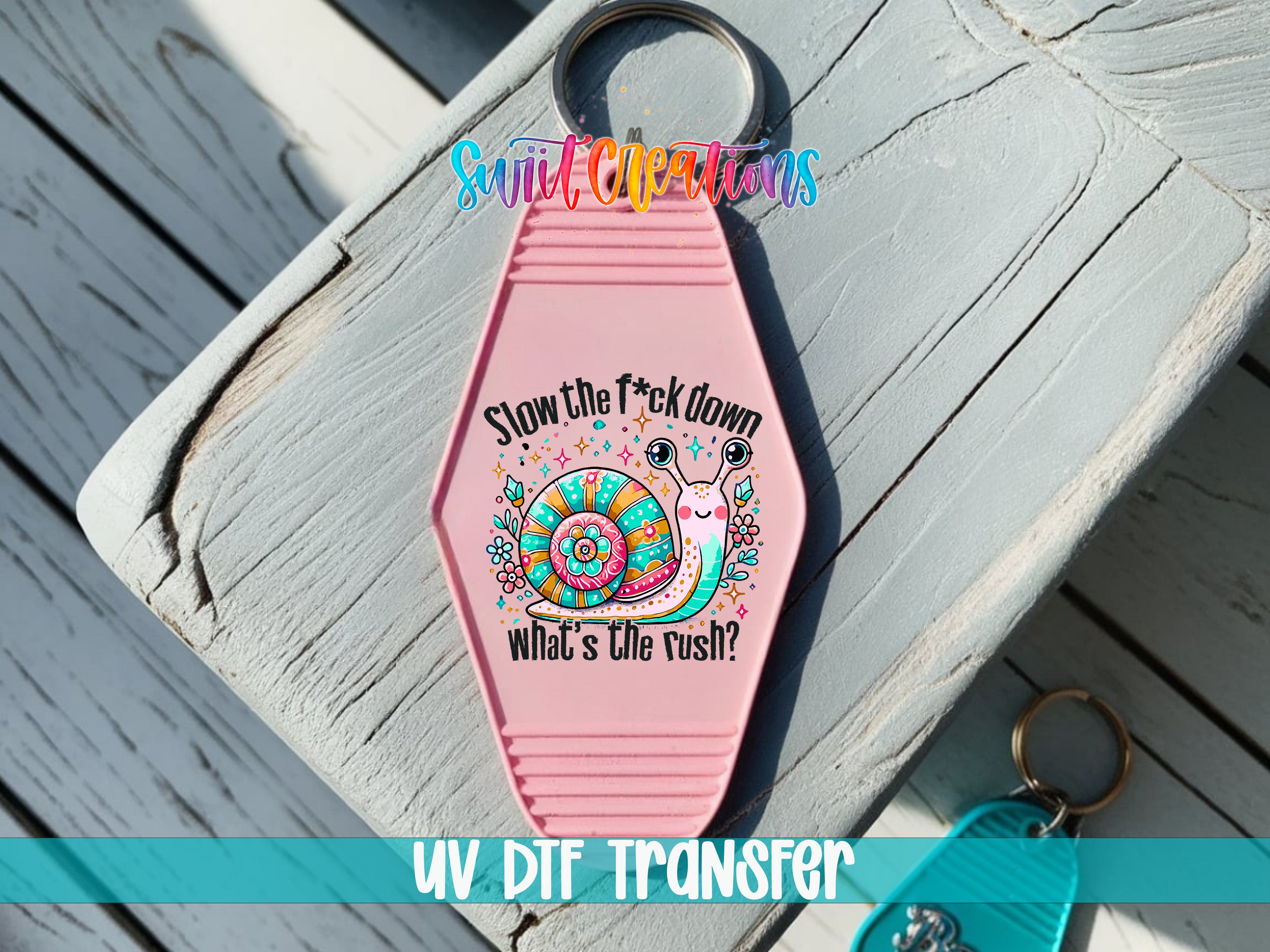 A pink keychain with a colorful snail design and text that says "Slow the fuck down What's the rush?"
