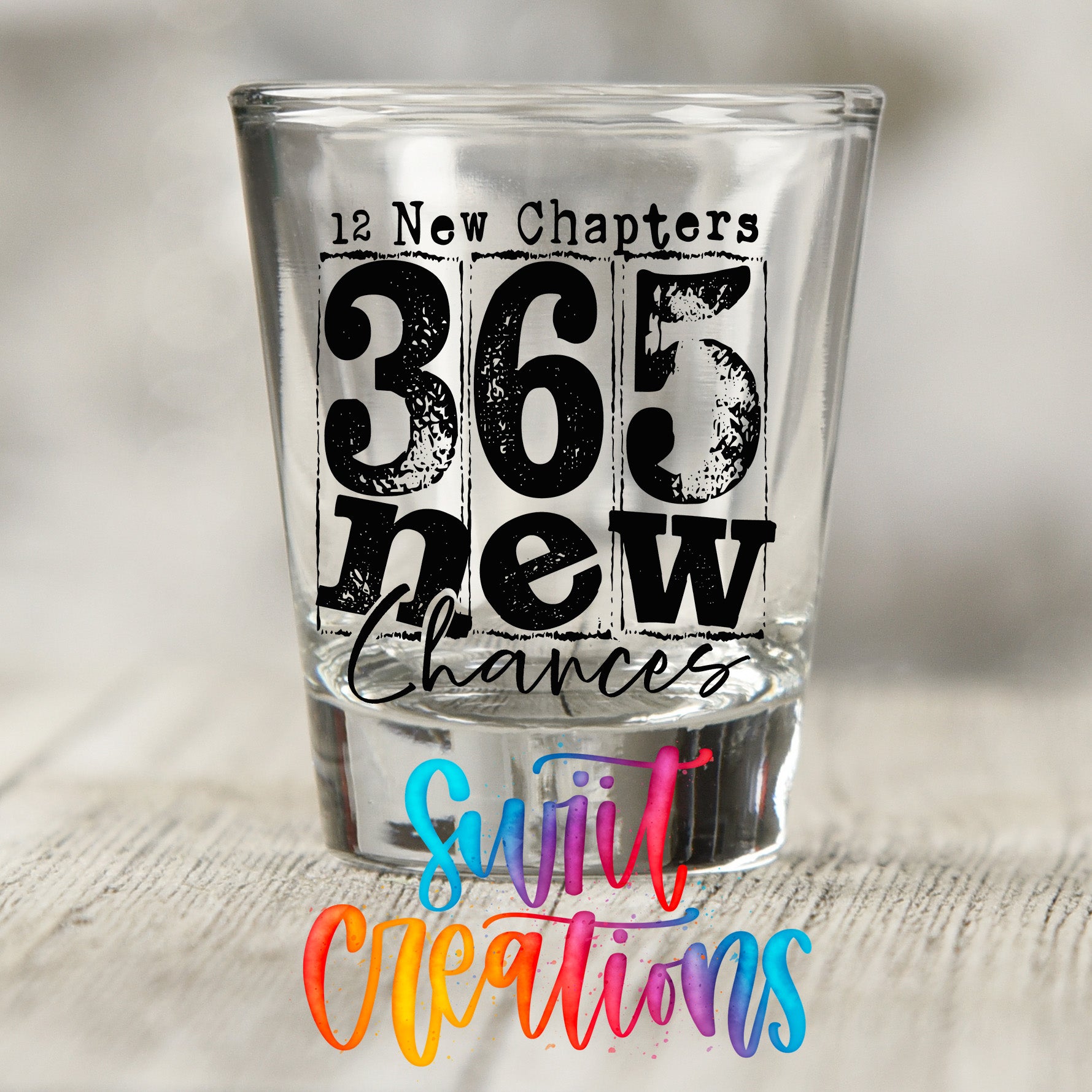 A shot glass with the text "12 New Chapters 365 new chances" printed on it, along with a colorful watermark that says "Sjiv Creation" below the text.