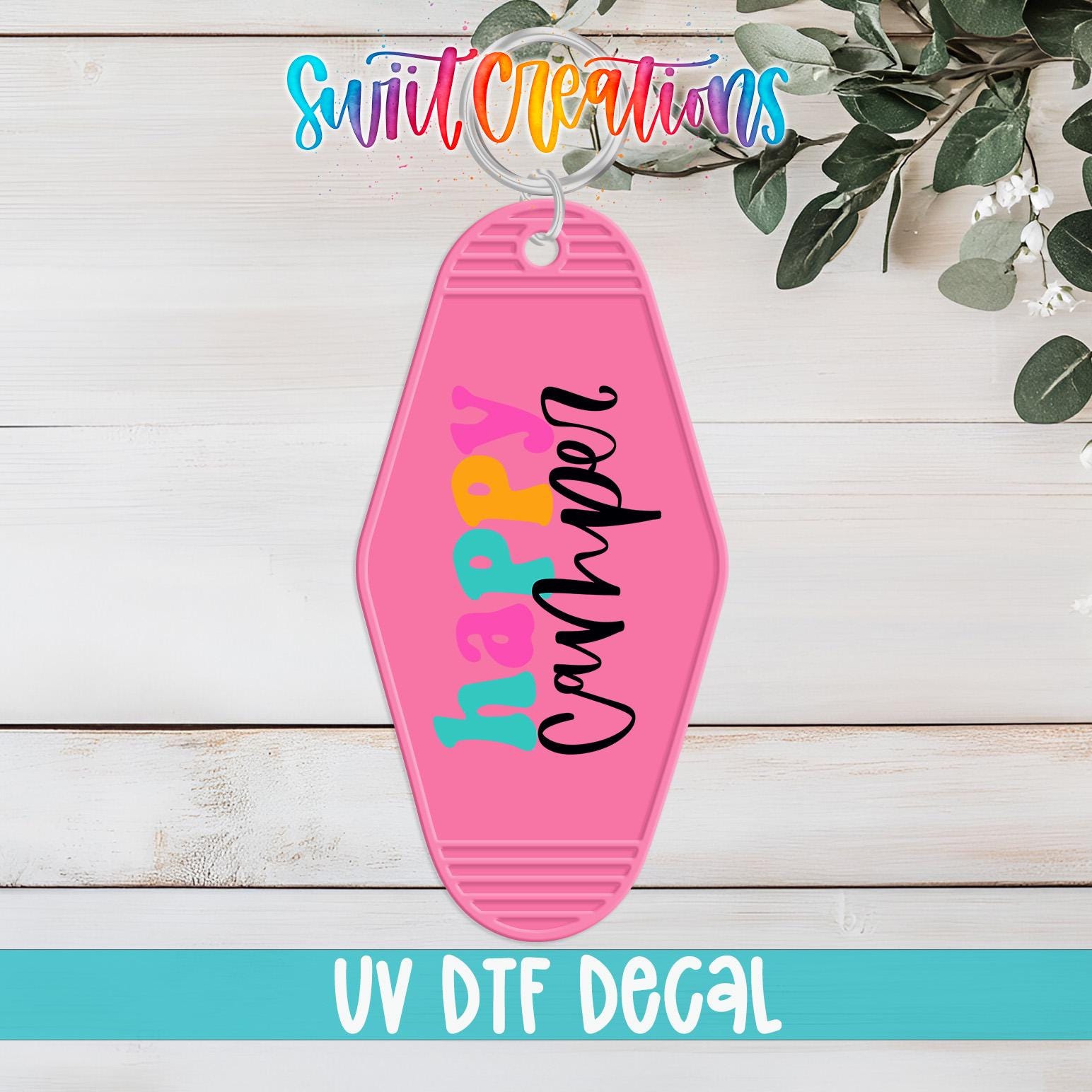 A pink keychain with the text "hAPPY CANHPER" printed on it, hanging on a wooden surface with some greenery in the background.