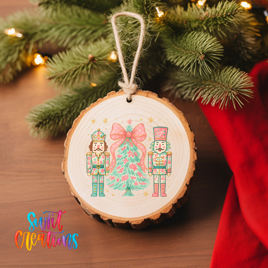 A wooden ornament featuring two nutcracker characters, one on each side of a Christmas tree, is hanging on a tree branch with twinkling lights in the background.
