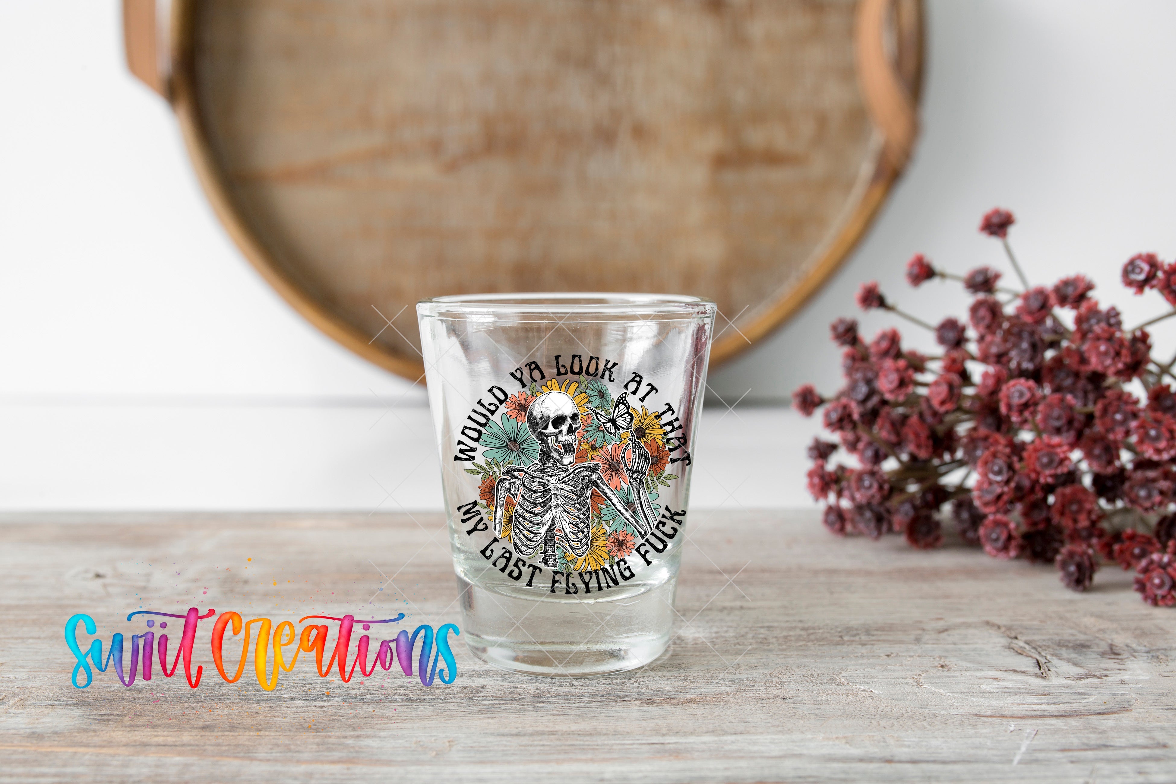 a shot glass sitting on a table next to some flowers