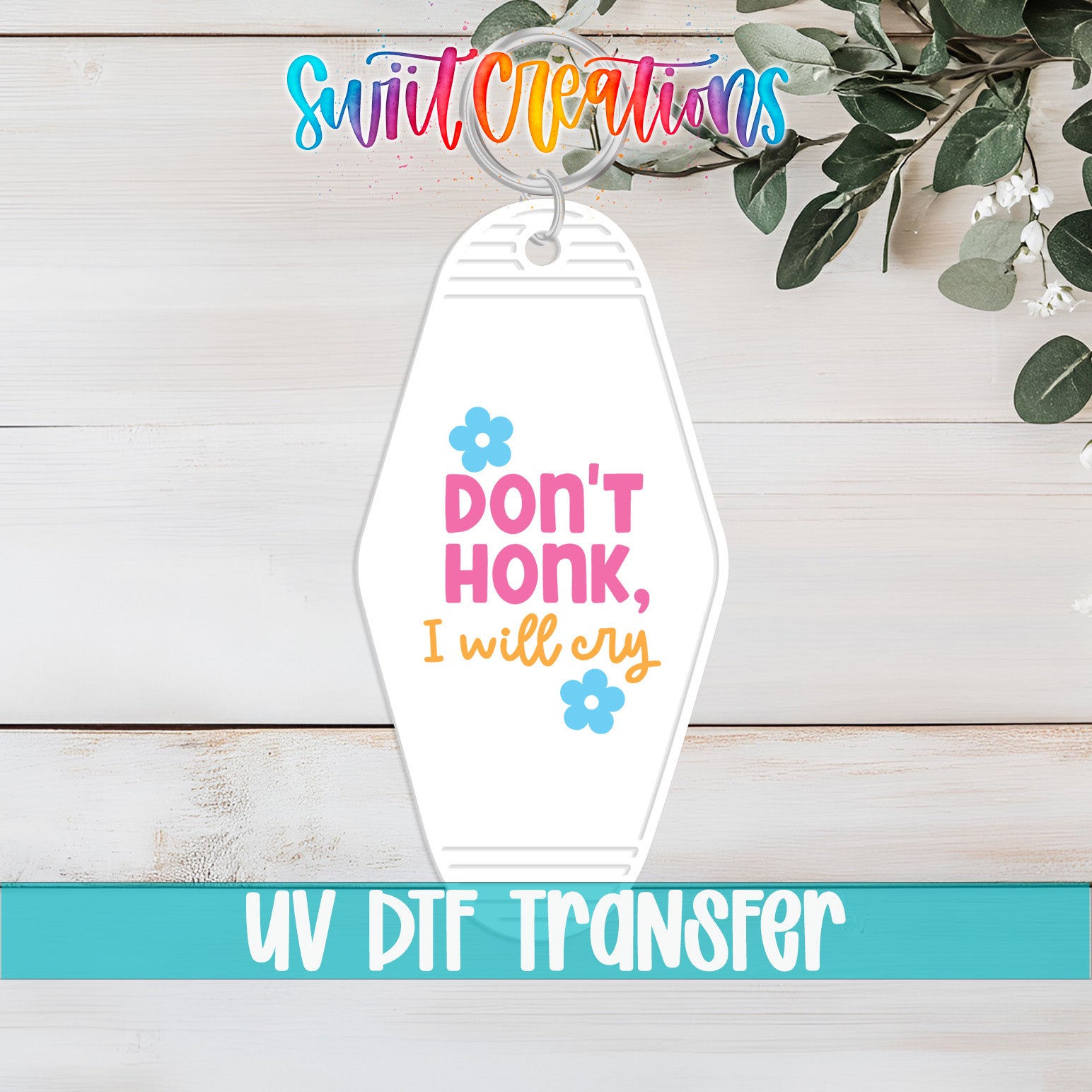 A keychain with a message that says "Don't honk, I will cry" and a small flower design. The keychain is placed on a wooden surface, and there is a plant in the background.