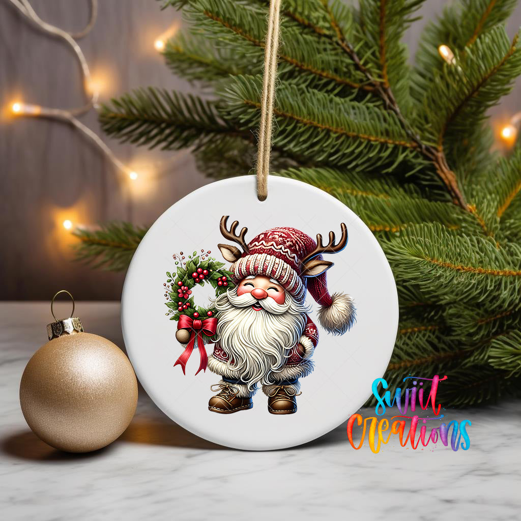 A white ceramic ornament featuring a Santa Claus figure holding a wreath and a gold ornament, placed on a marble surface with a Christmas tree in the background.