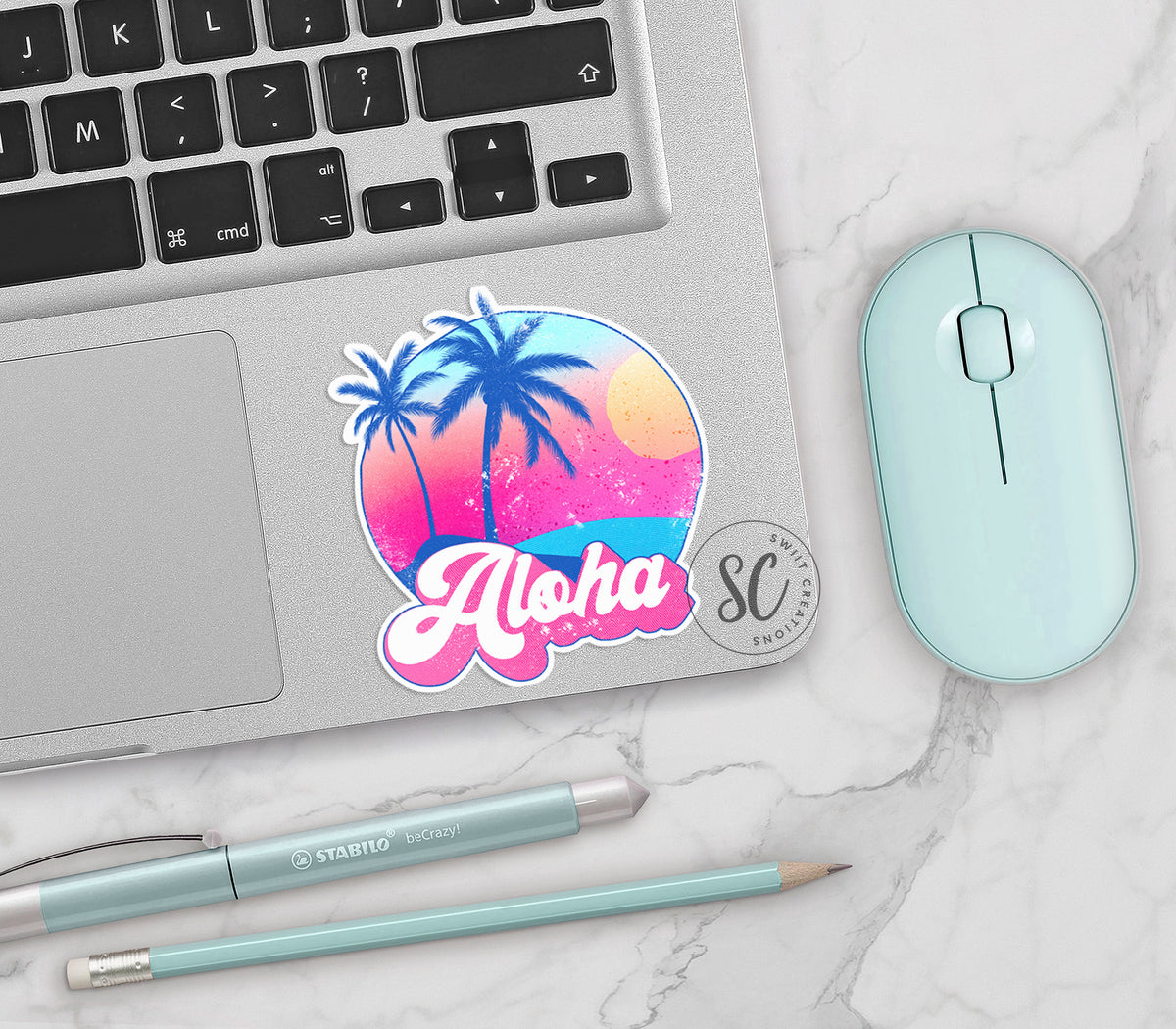 Aloha vinyl sticker on a silver laptop next to a mint mouse and pens