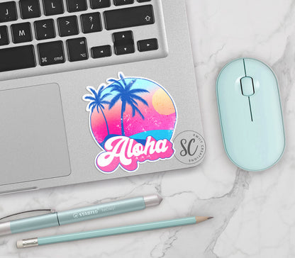 Aloha vinyl sticker on a silver laptop next to a mint mouse and pens