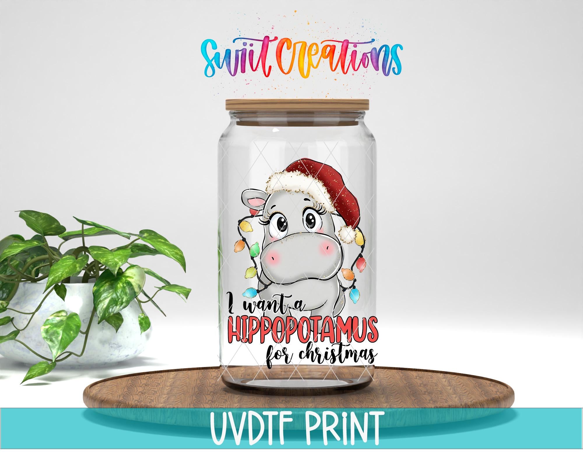 A glass jar with a cartoon image of a hippopotamus wearing a Santa hat, along with text that says "I want a Hippopotamus for Christmas". The jar is placed on a wooden surface, and there is a potted plant in the background.