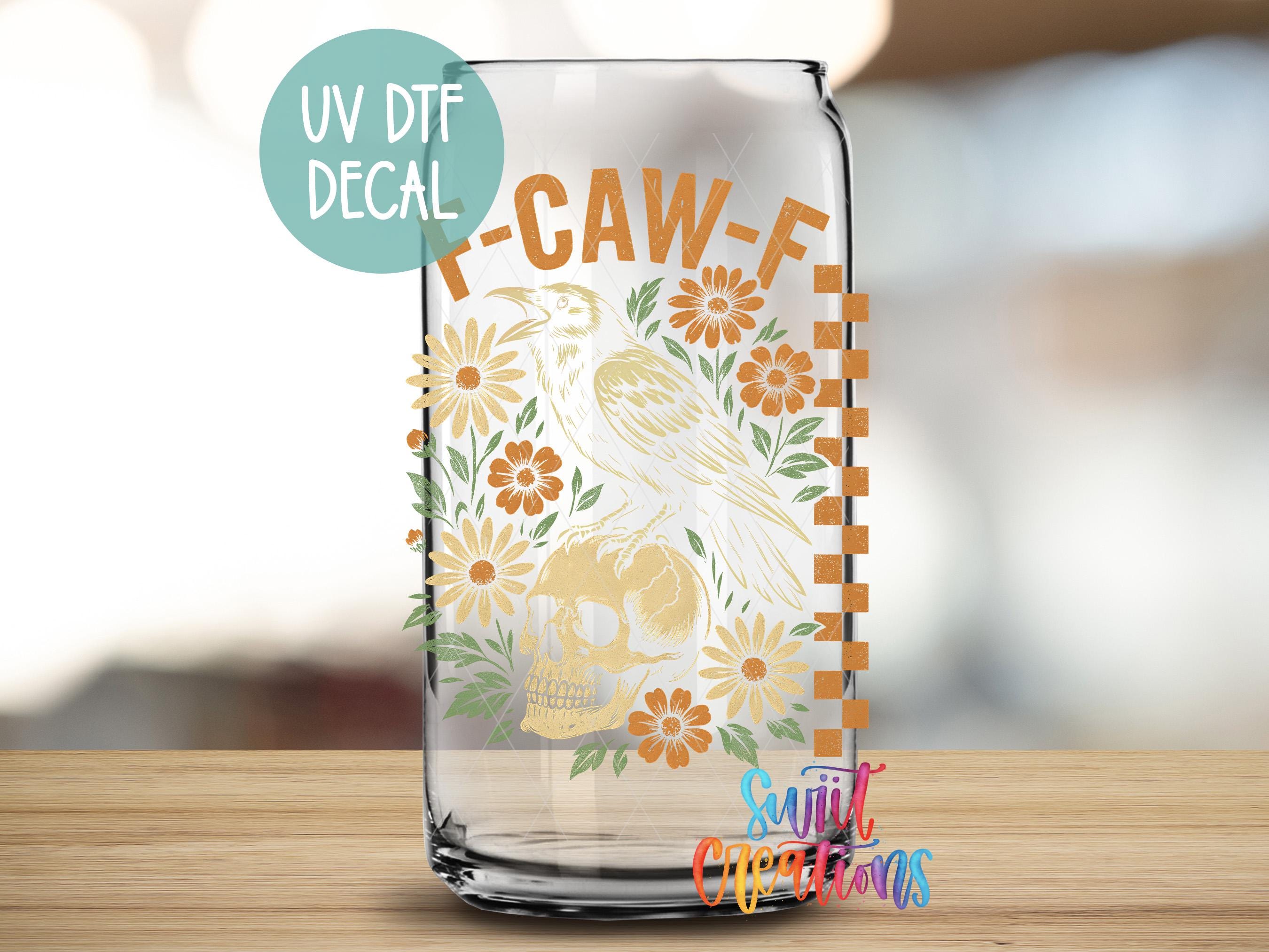 A glass can with a UV decal featuring a bird and flowers, along with text that reads "UV UV DTF DECAL" and "T-CAW-F".