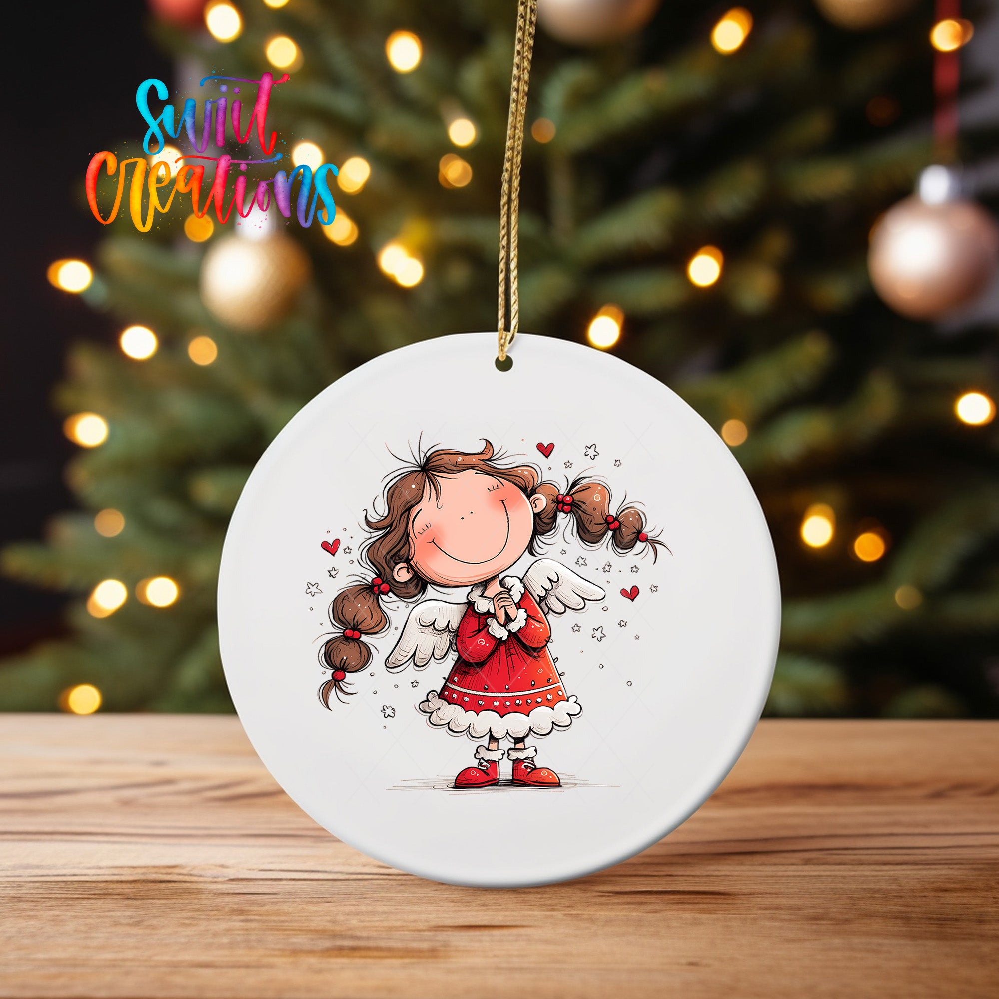 A white ceramic ornament featuring a smiling girl with long hair and wings, surrounded by stars, is displayed on a wooden surface in front of a blurred Christmas tree.