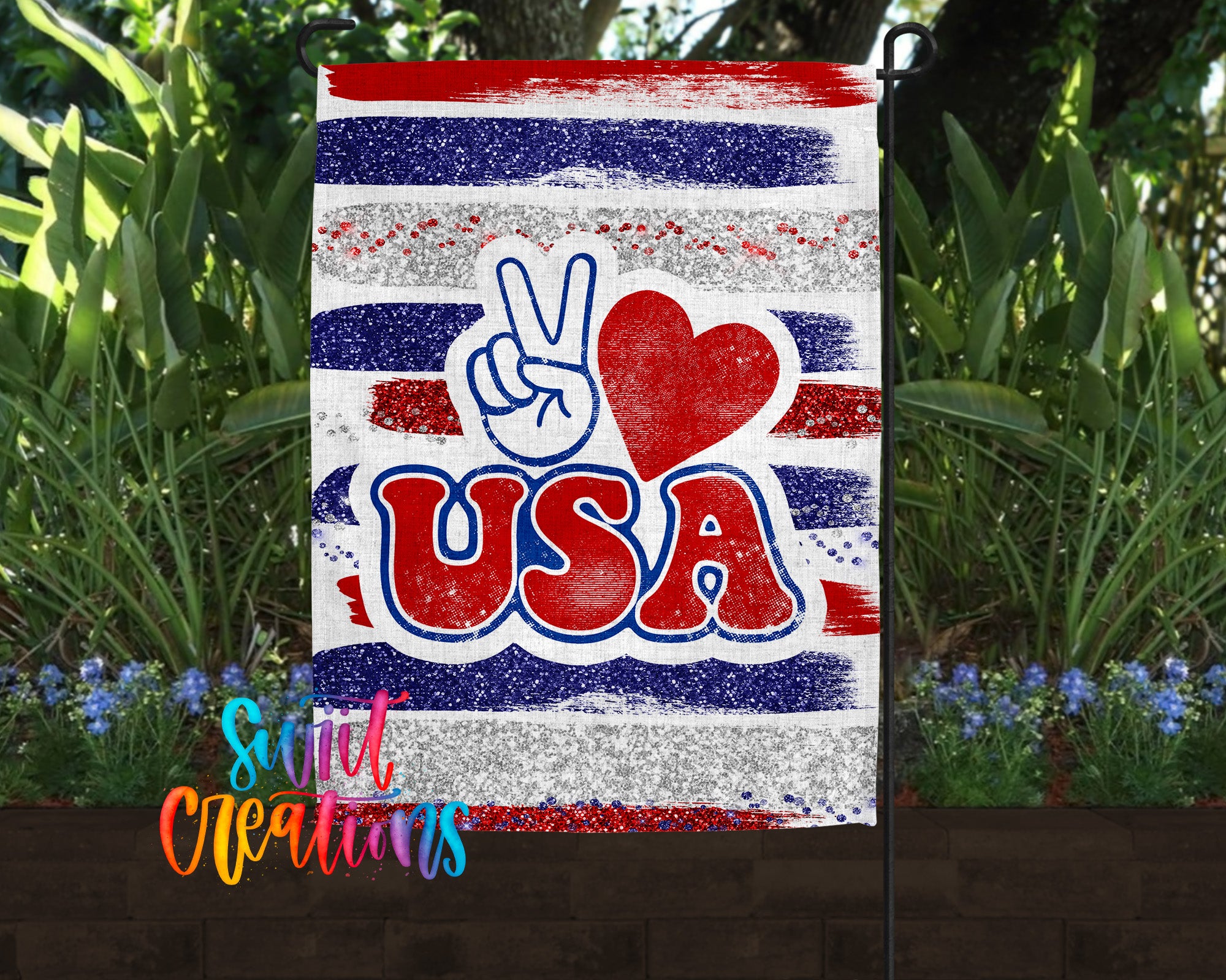 A patriotic flag with the text "I ♥ USA" and a peace sign graphic, surrounded by a lush garden with green plants and blue flowers.
