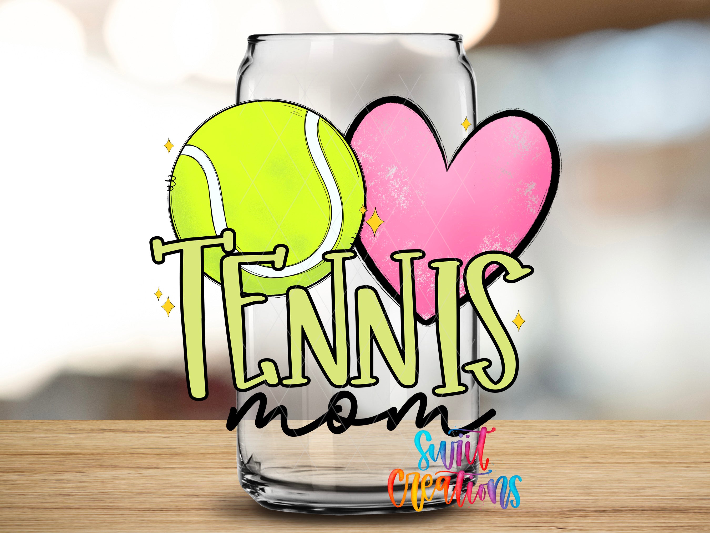 A glass with a tennis ball and a heart on it, along with the text "TENNIS mom" and "Suntory Creations" written on it.