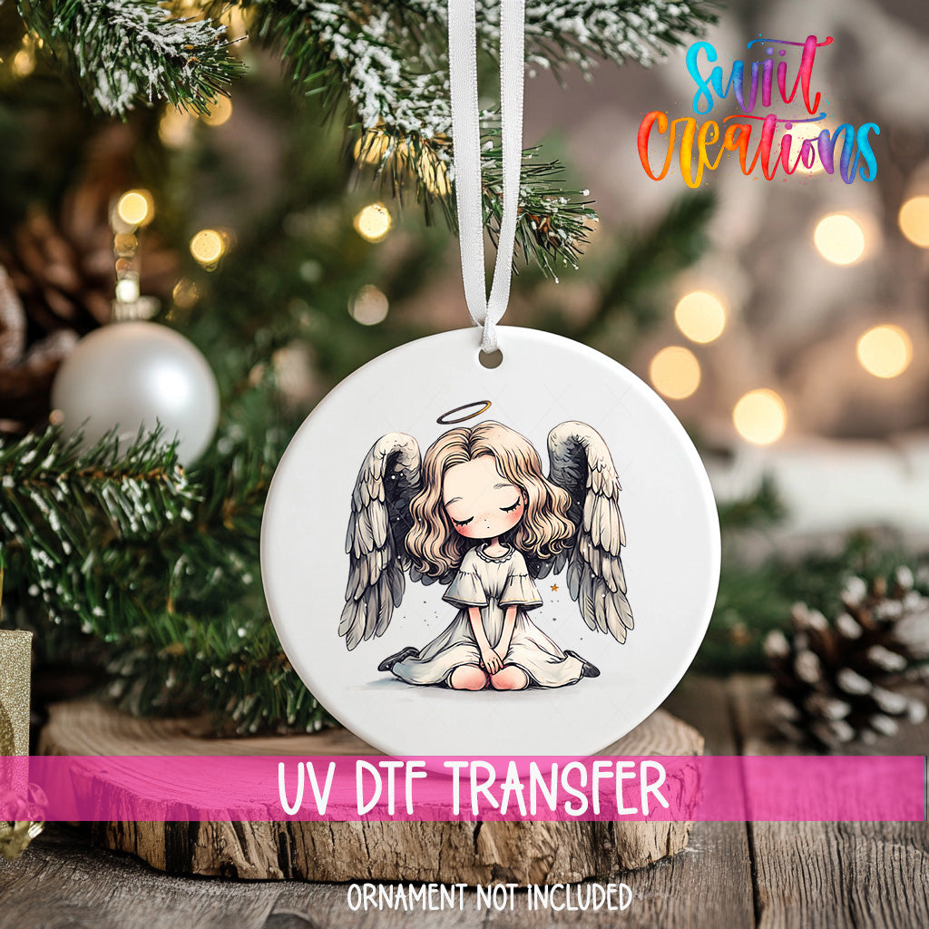 A white ceramic ornament with a cartoon illustration of a smiling angel with wings, hanging on a Christmas tree.