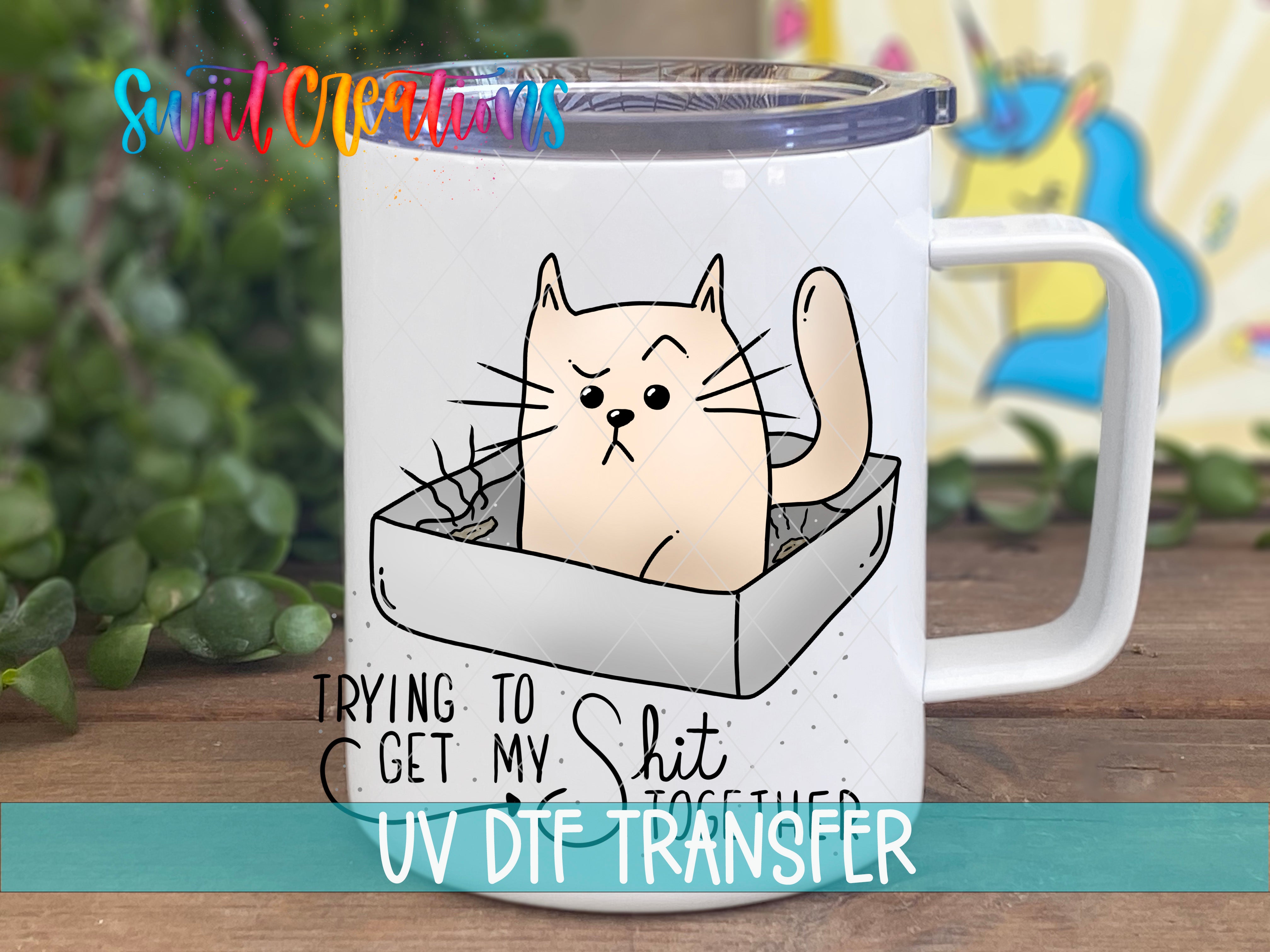 A white mug with a cartoon cat illustration and text that says "Trying to Get My Shit Together" and "UV DFT Transfer".
